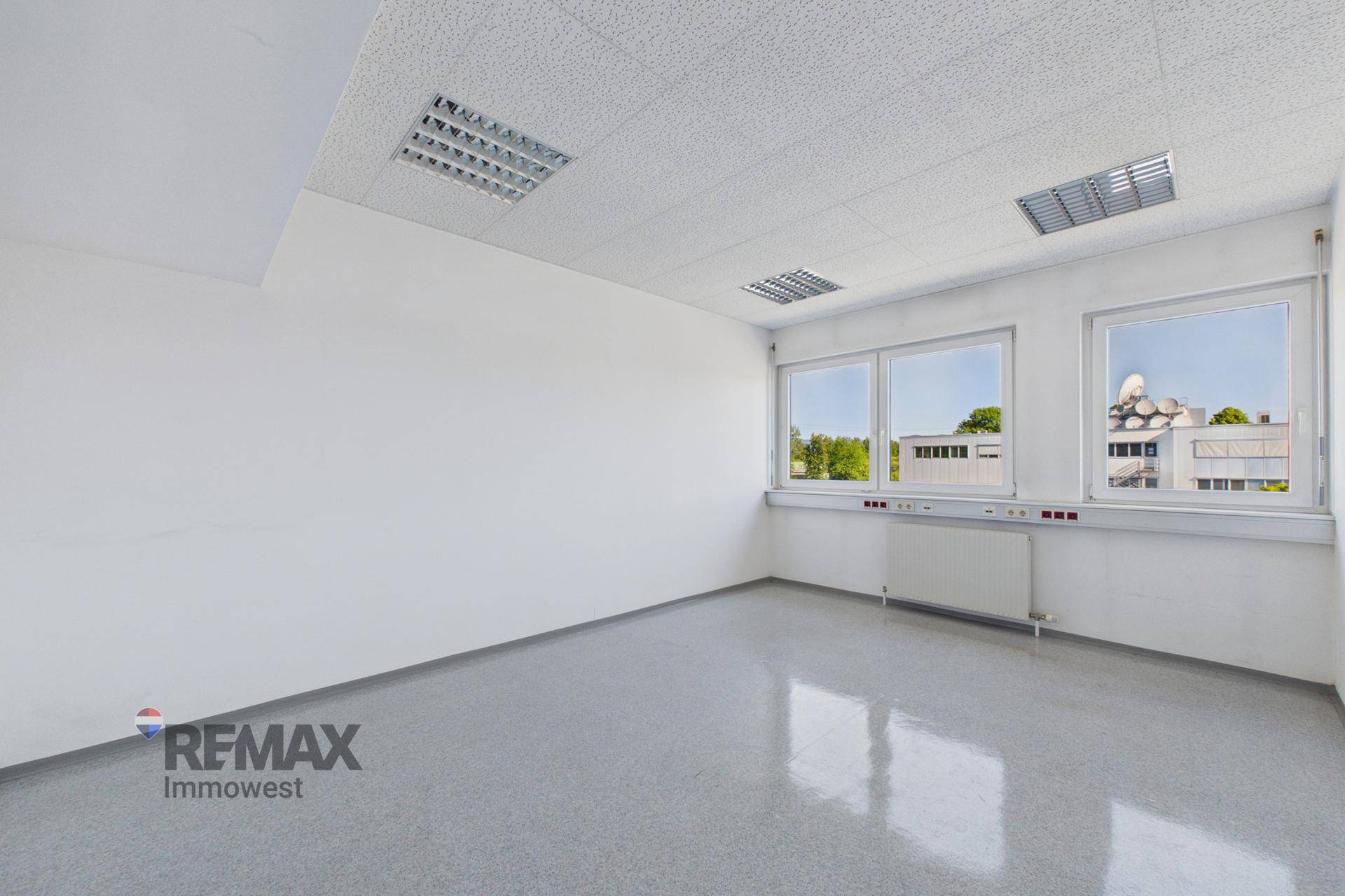 Helles Büro mit glänzendem grauem Boden, großen Fenstern und Deckenbeleuchtung, ideal für Arbeitsbereiche.