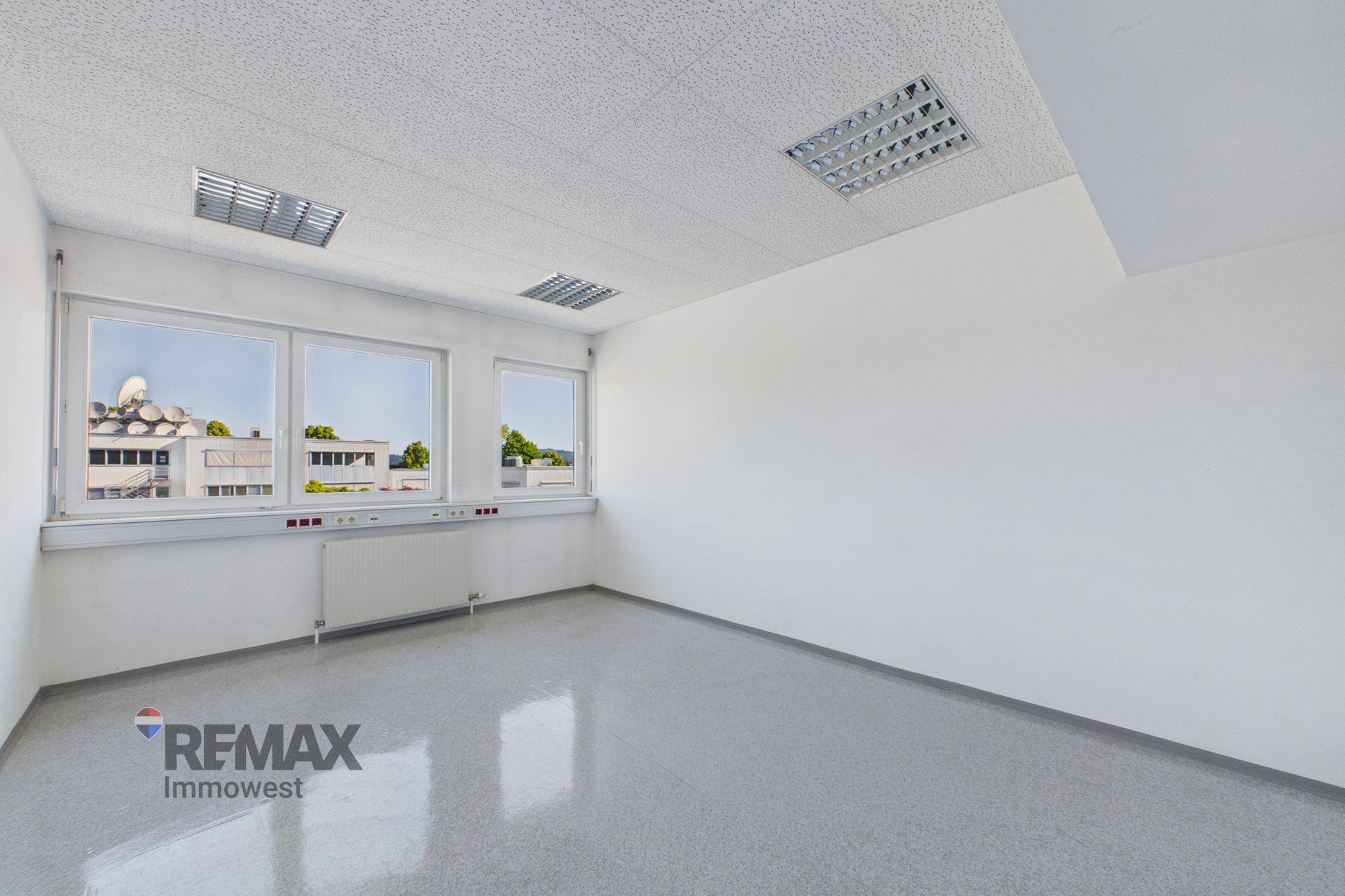 Geräumiges Büro mit glänzendem grauem Boden und großen Fenstern, die viel Tageslicht hereinlassen.
