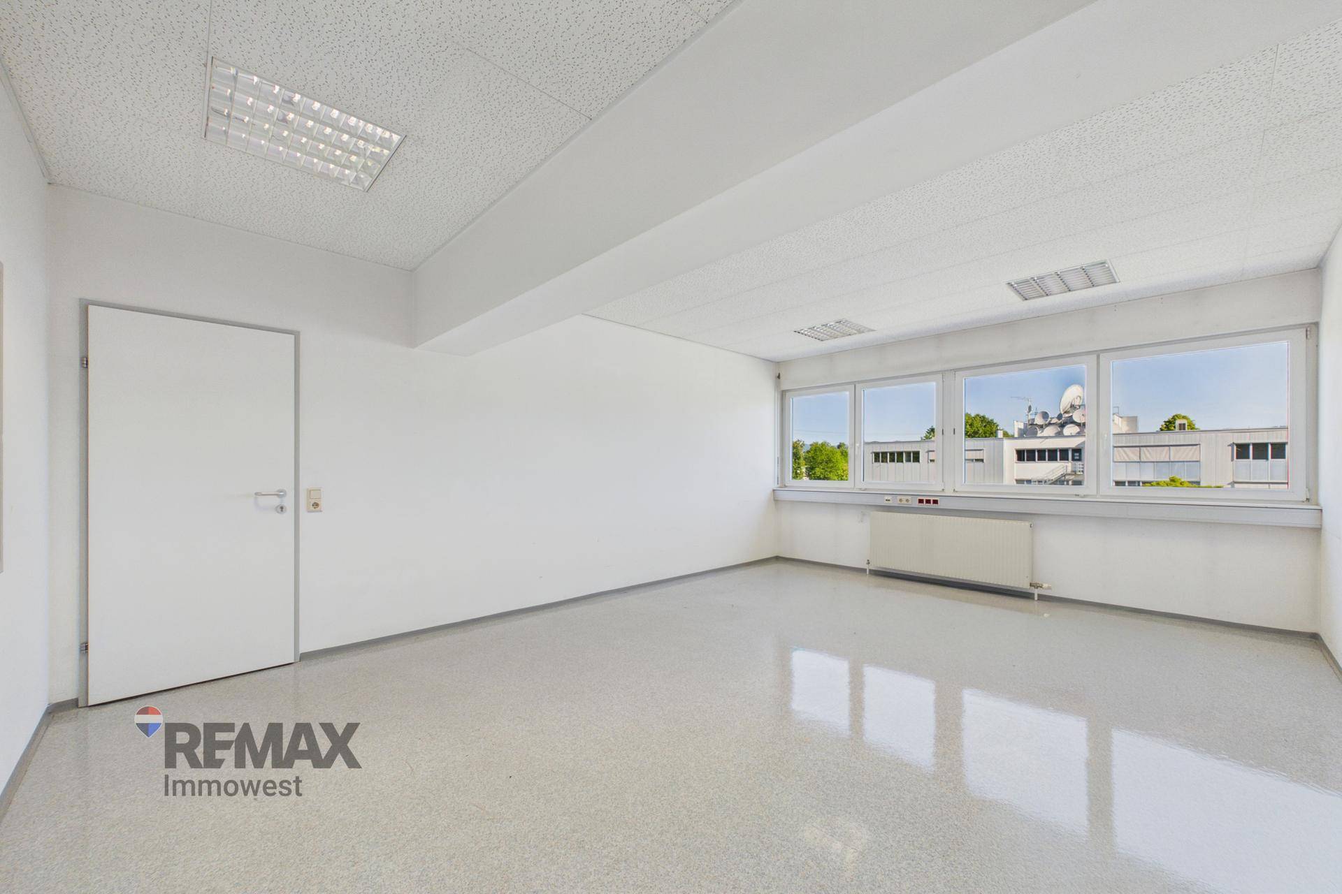 Helles Büro mit glänzendem grauem Boden, weißer Tür und großen Fenstern für optimale Belichtung.