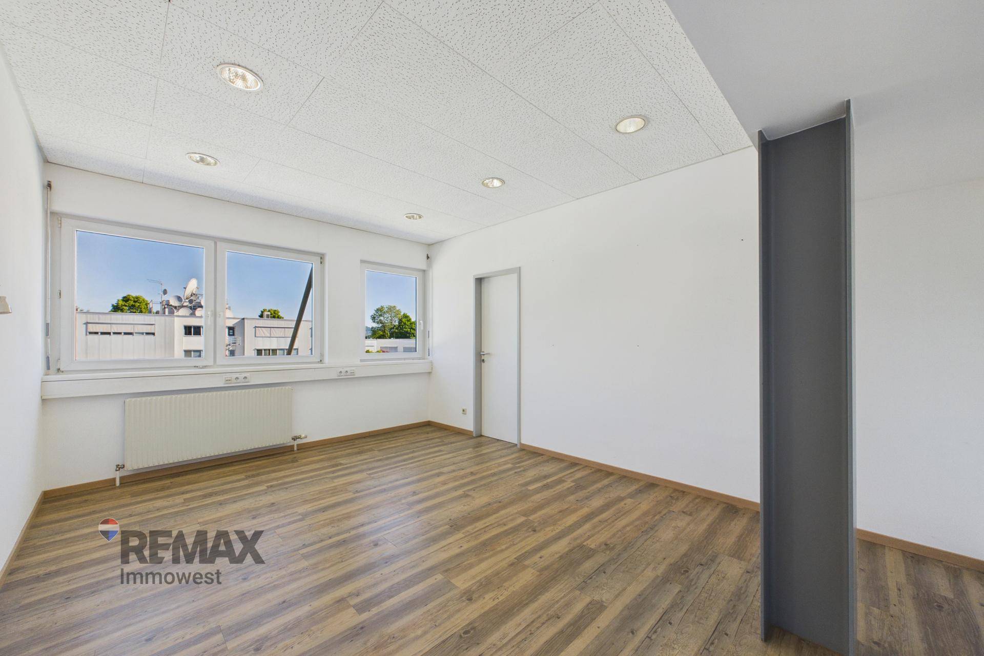 Helles Büro mit Holzboden, großen Fenstern und weiß gestrichenen Wänden, bietet viel Tageslicht.