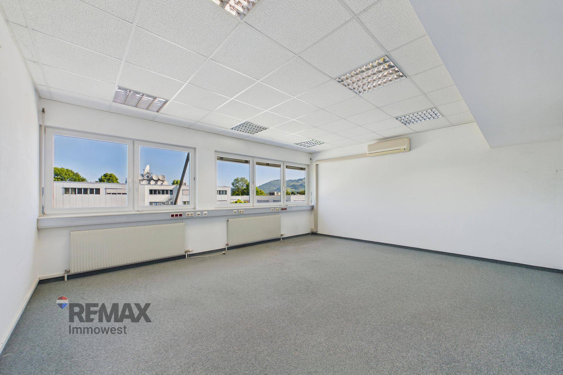 Geräumiges Büro mit grauem Teppichboden, großen Fenstern und Klimaanlage für angenehmes Raumklima.