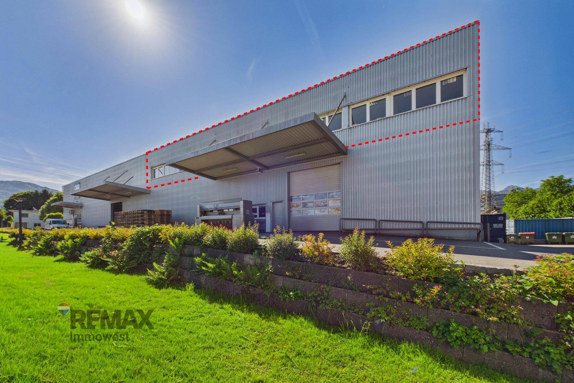 Seitenansicht des Industriegebäudes mit gepflegter Grünanlage und Laderampen unter blauem Himmel.