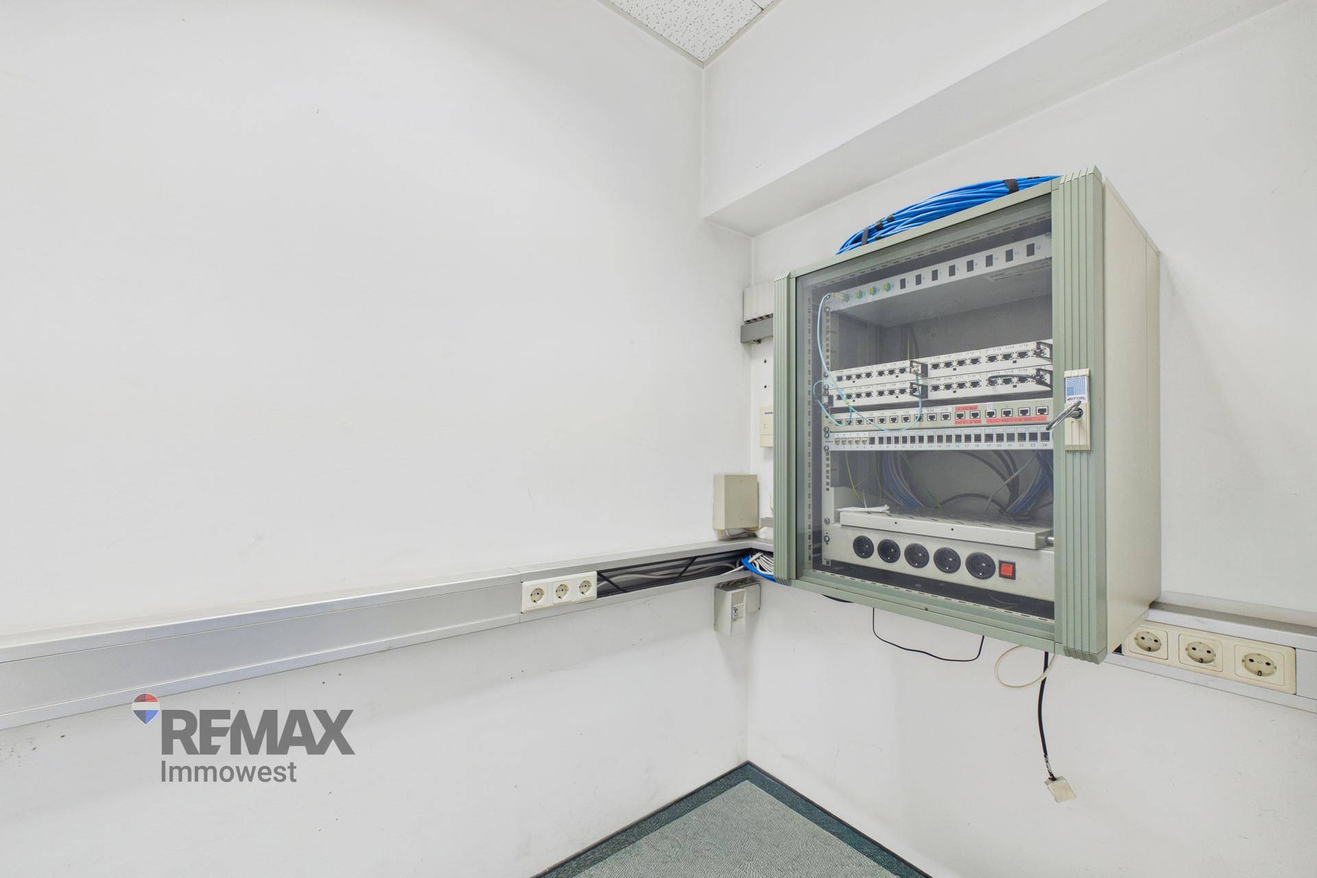 Ecke eines Büros mit einem Netzwerkschrank und zahlreichen Steckdosen, ideal für IT-Infrastruktur.