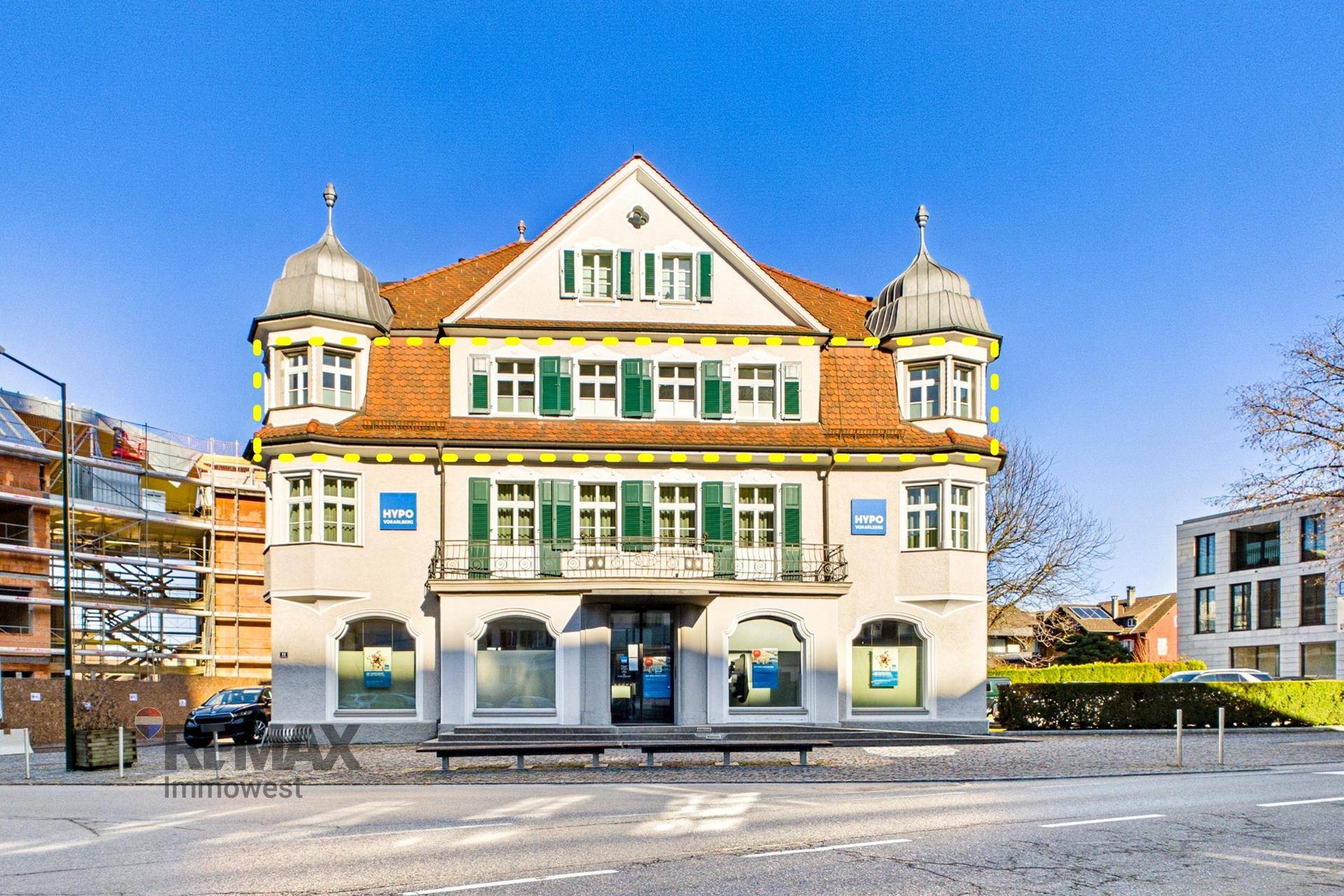 Historisches Gebäude mit markanter Architektur, Erkern und grünen Fensterläden unter blauem Himmel.