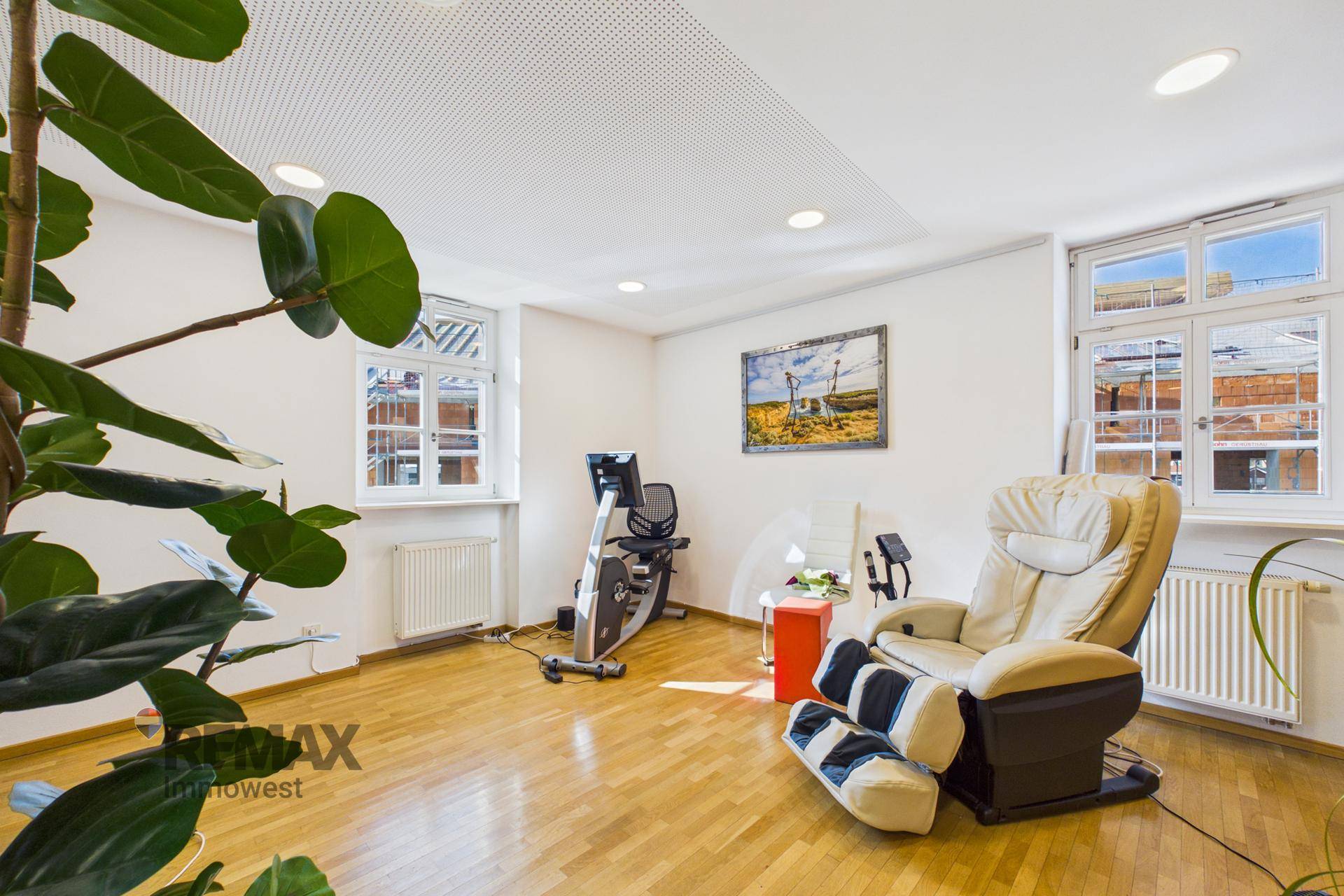 Geräumiger Therapieraum mit Trainingsgeräten, Massagesessel und großen Fenstern für viel Licht.