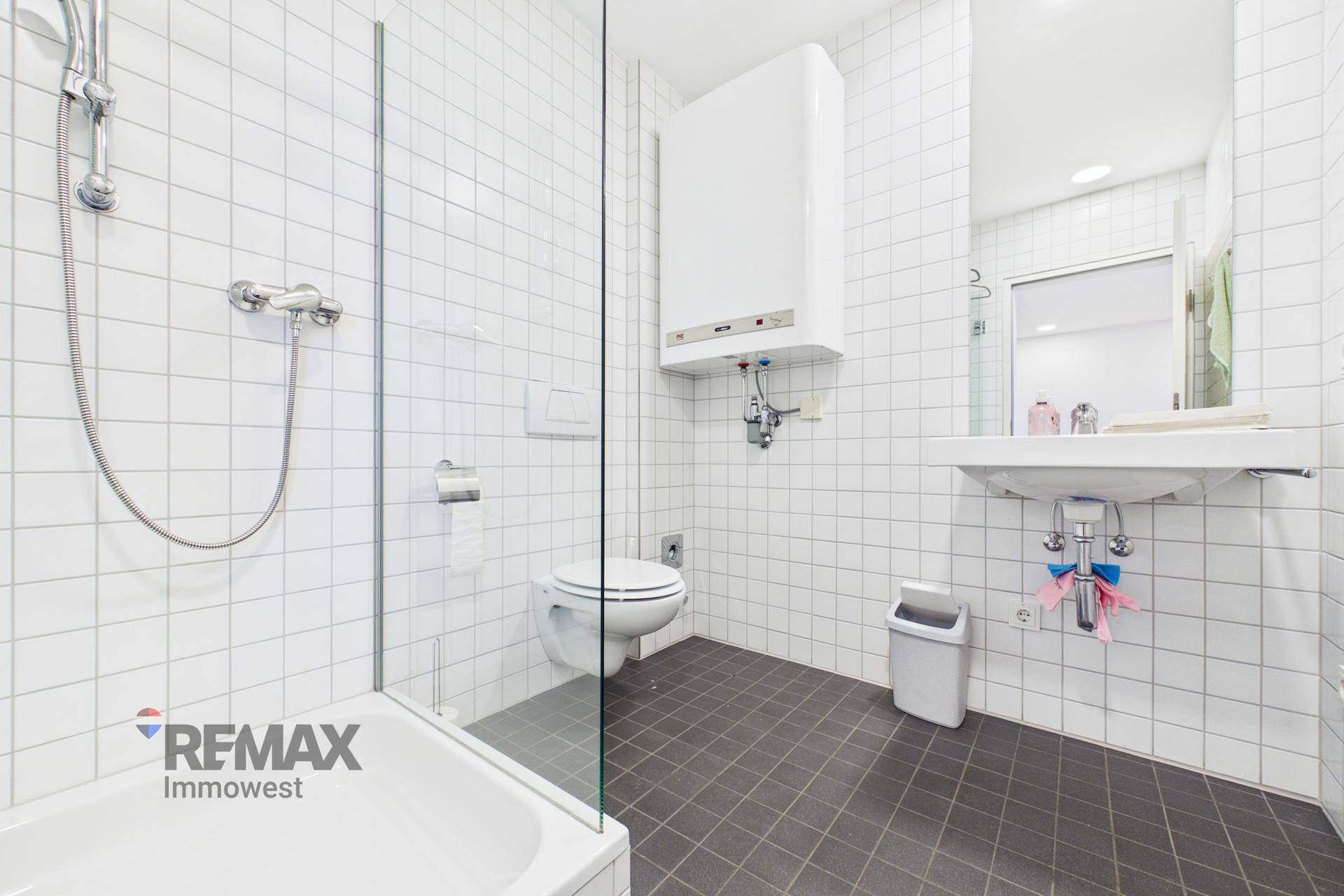 Modernes Badezimmer mit weißen Fliesen, Dusche, WC und Waschbecken, sauber und funktional.