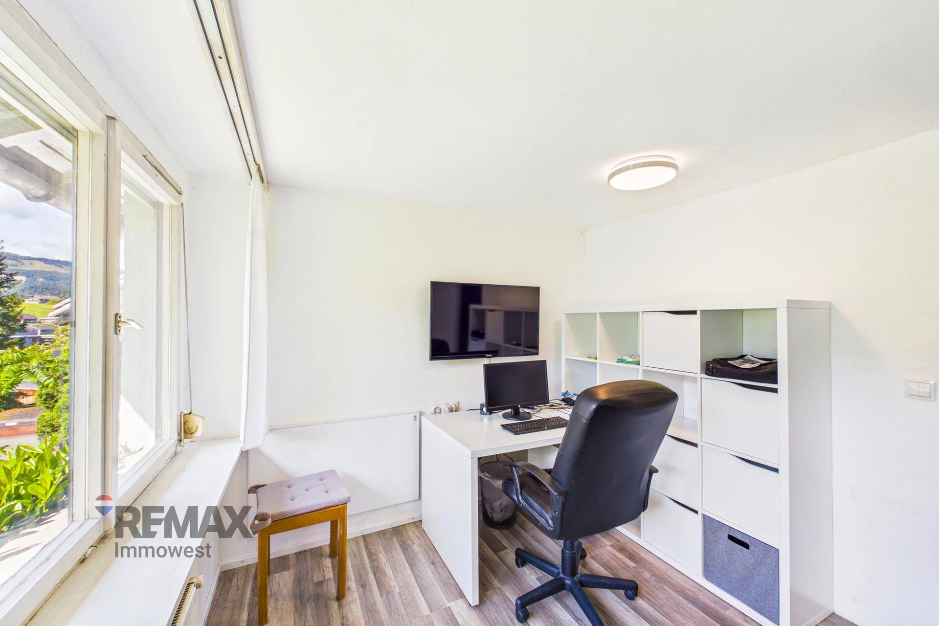 Helles Arbeitszimmer mit Schreibtisch, Bürostuhl und Fenster mit Blick ins Grüne.