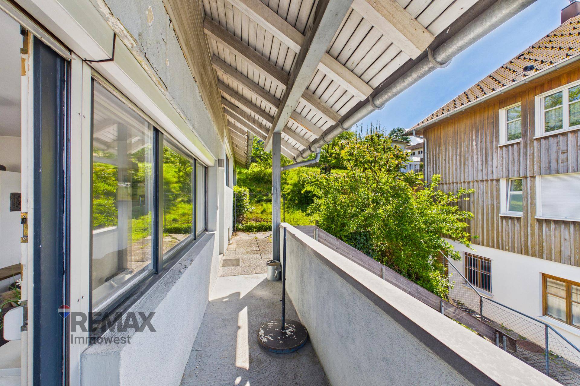 Überdachter Balkon mit Betonboden und Blick auf die grüne Umgebung und Nachbarhäuser.