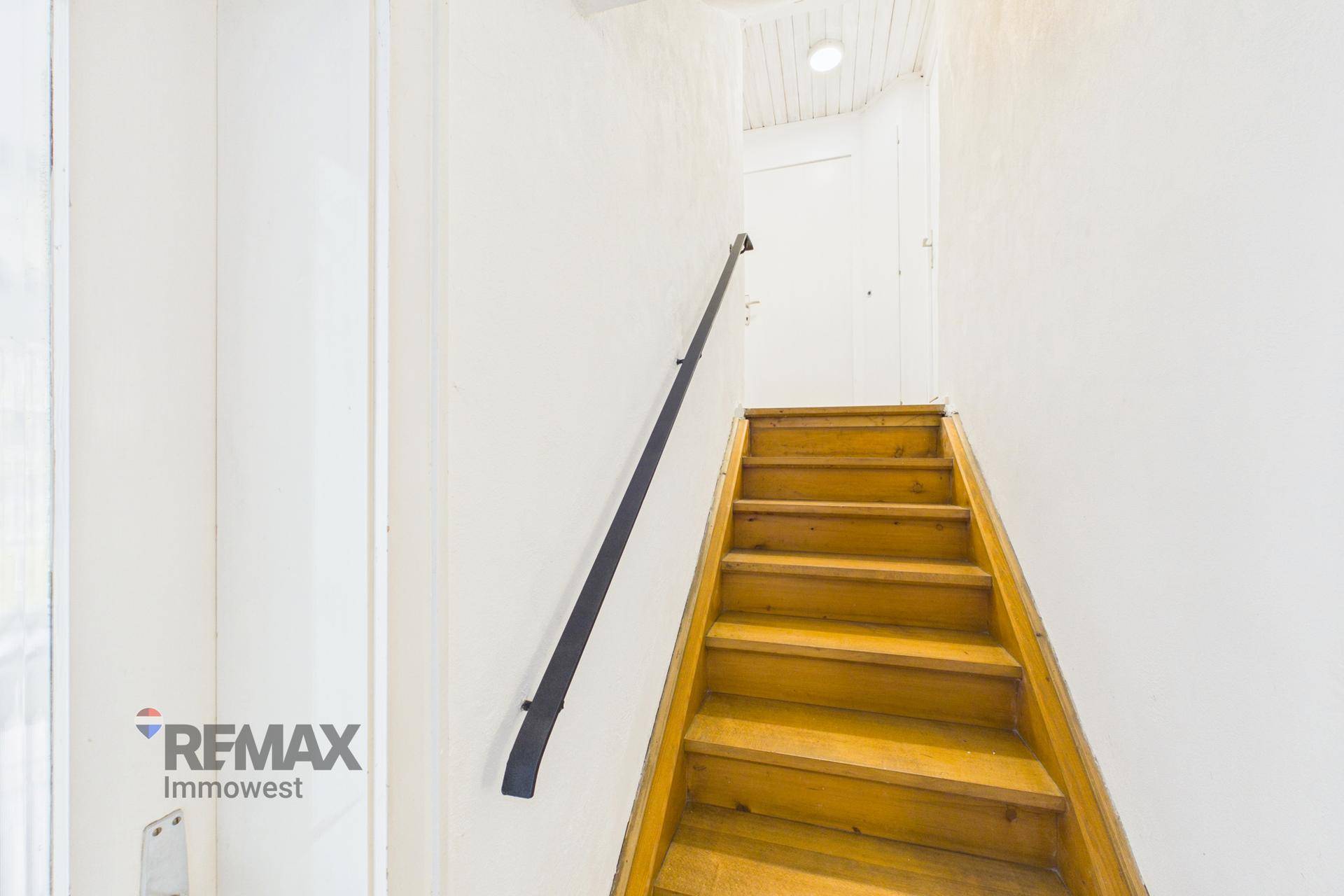 Holztreppe mit Geländer führt in ein oberes Stockwerk.