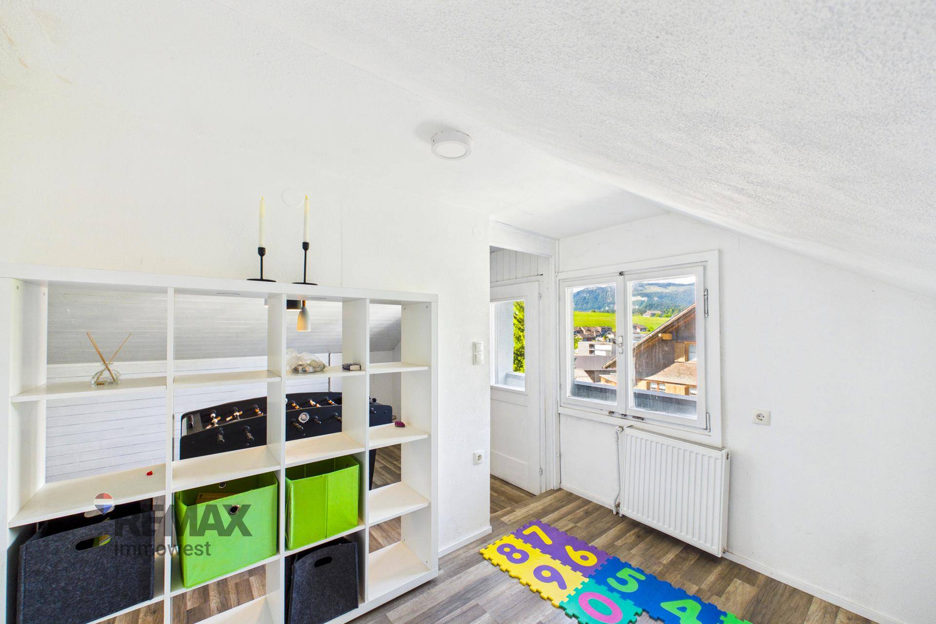 Heller Dachbodenraum mit Spielbereich, Regal und Blick auf die Landschaft.