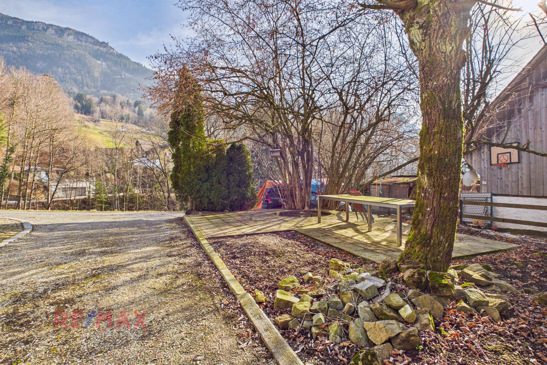 Gemütlicher Außenbereich mit Holztisch und Bänken unter Bäumen, ideal für entspannte Stunden.