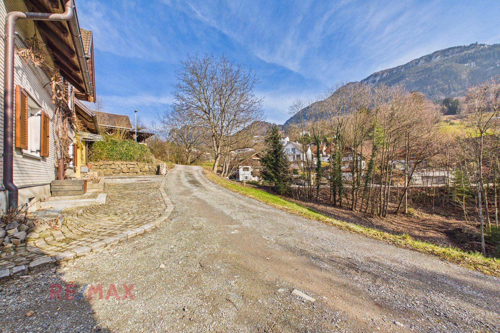 Schotterweg führt zum Haus hinauf, umgeben von Bäumen und mit Blick auf die Berge.