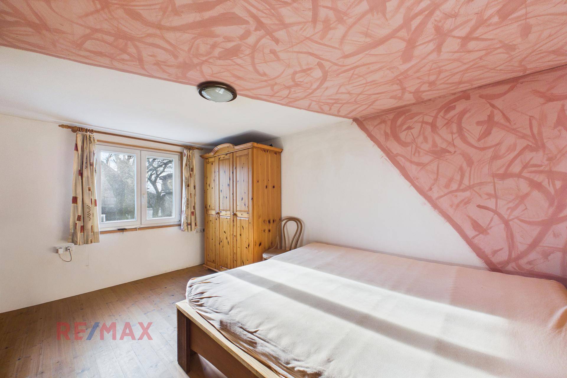 Helles Schlafzimmer mit Holzbett, Schrank und Fenster, das viel Tageslicht hereinlässt.