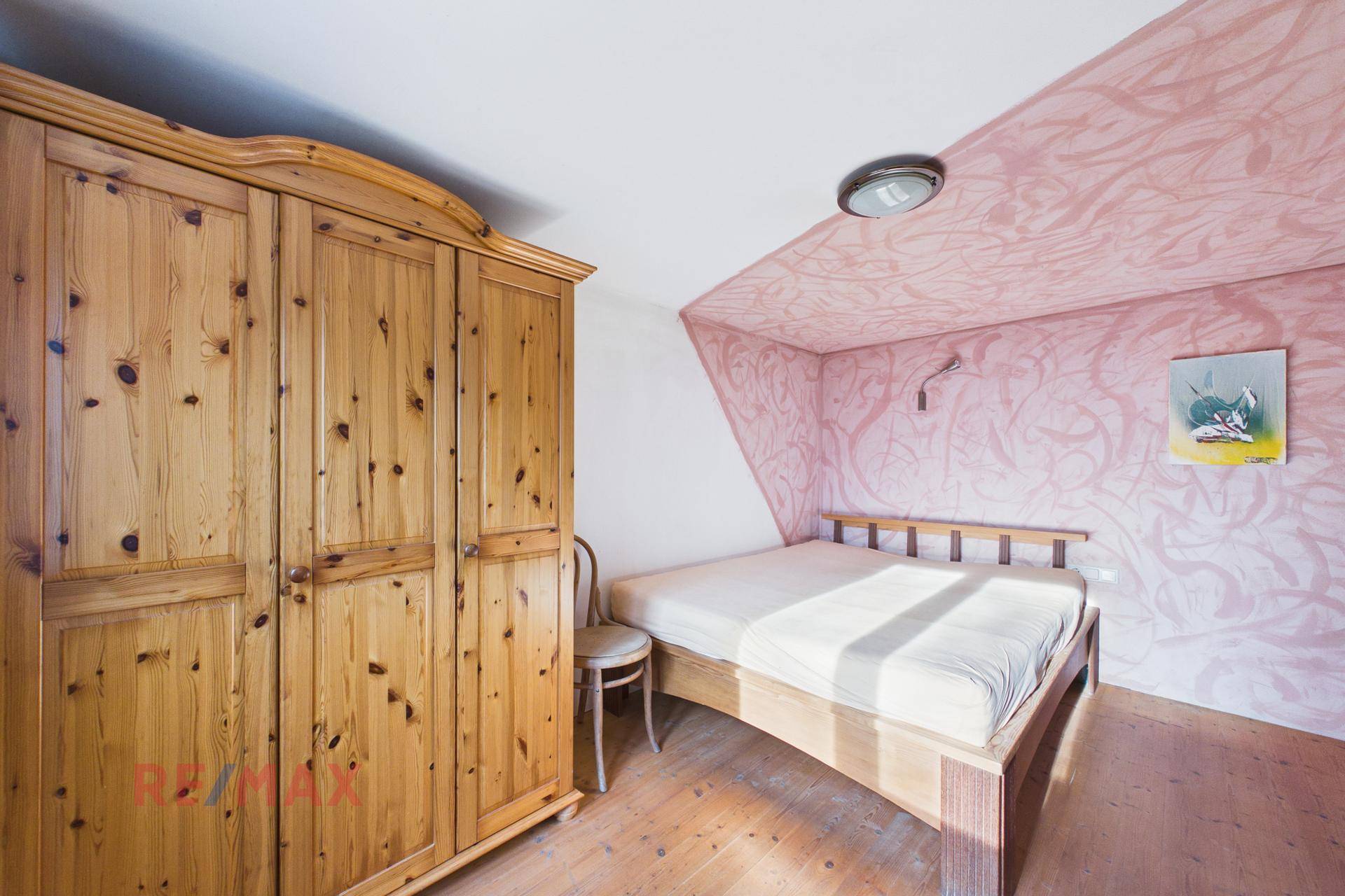 Schlafzimmer mit Holzbett, großem Holzschrank und einer auffälligen rosa Wandgestaltung.