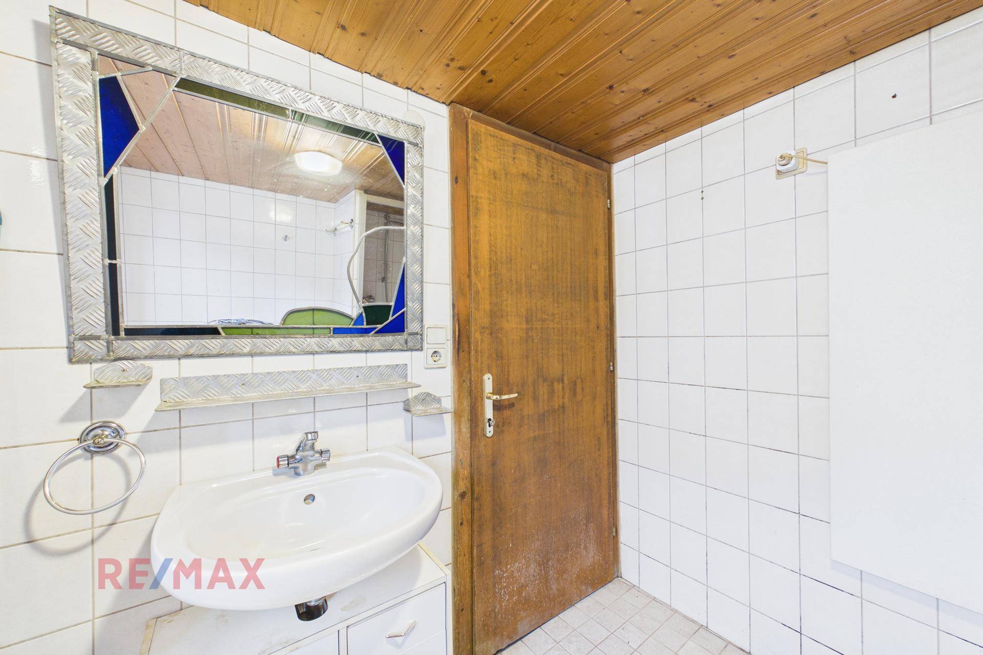 Badezimmer mit weiß gefliesten Wänden, Waschbecken und Holzdecke, ausgestattet mit Spiegel.