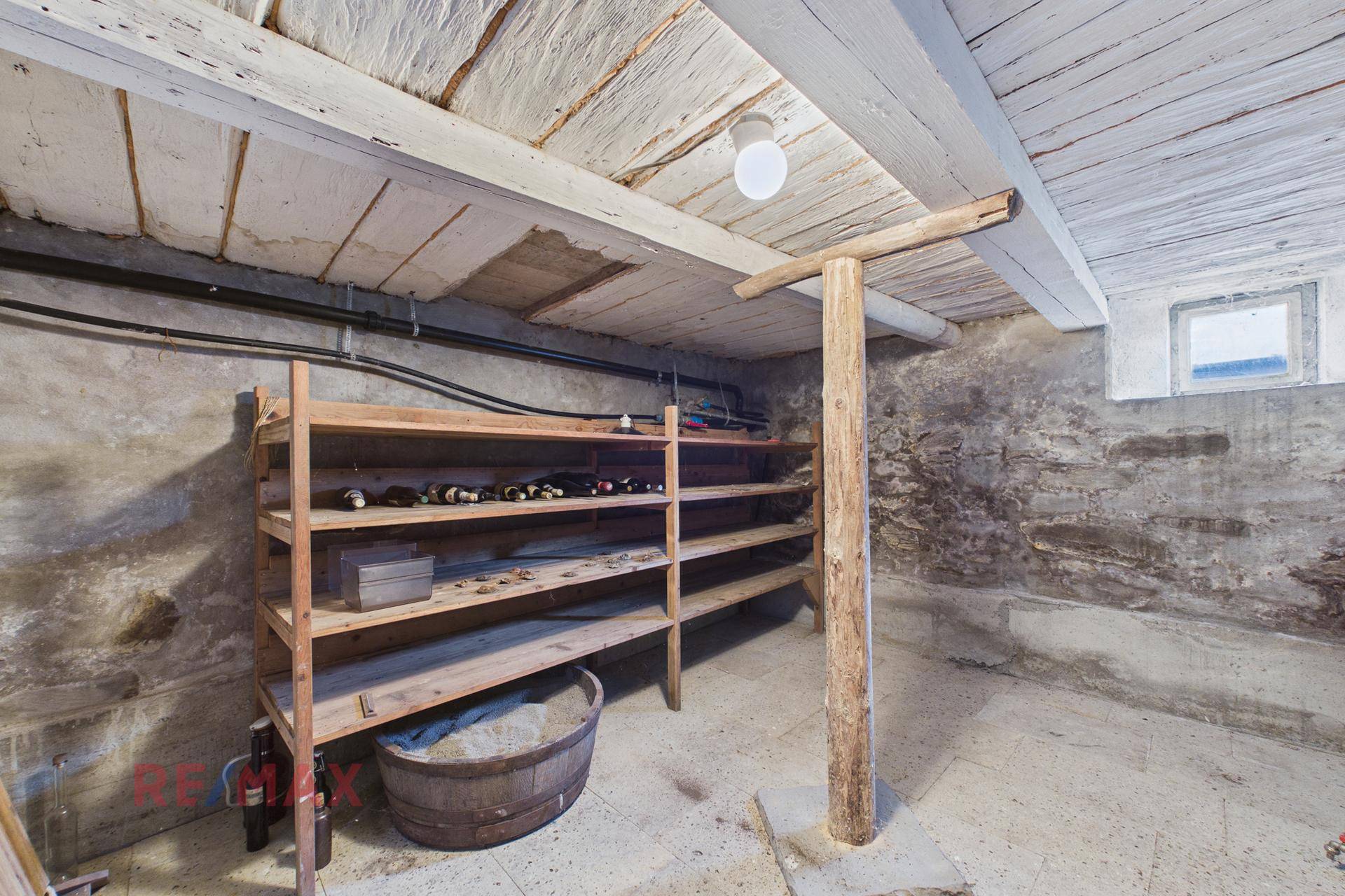 Rustikaler Weinkeller im Untergeschoss mit Holzregalen und Steinfundament, ideal zur Lagerung.