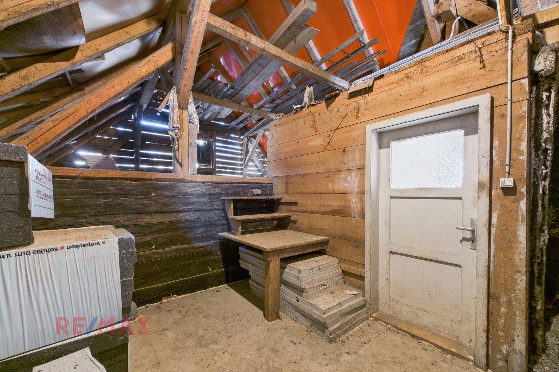 Teil des Dachbodens mit Holzwänden, einer Tür und sichtbarer Dachkonstruktion, bereit für Ausbau oder Lagerung.