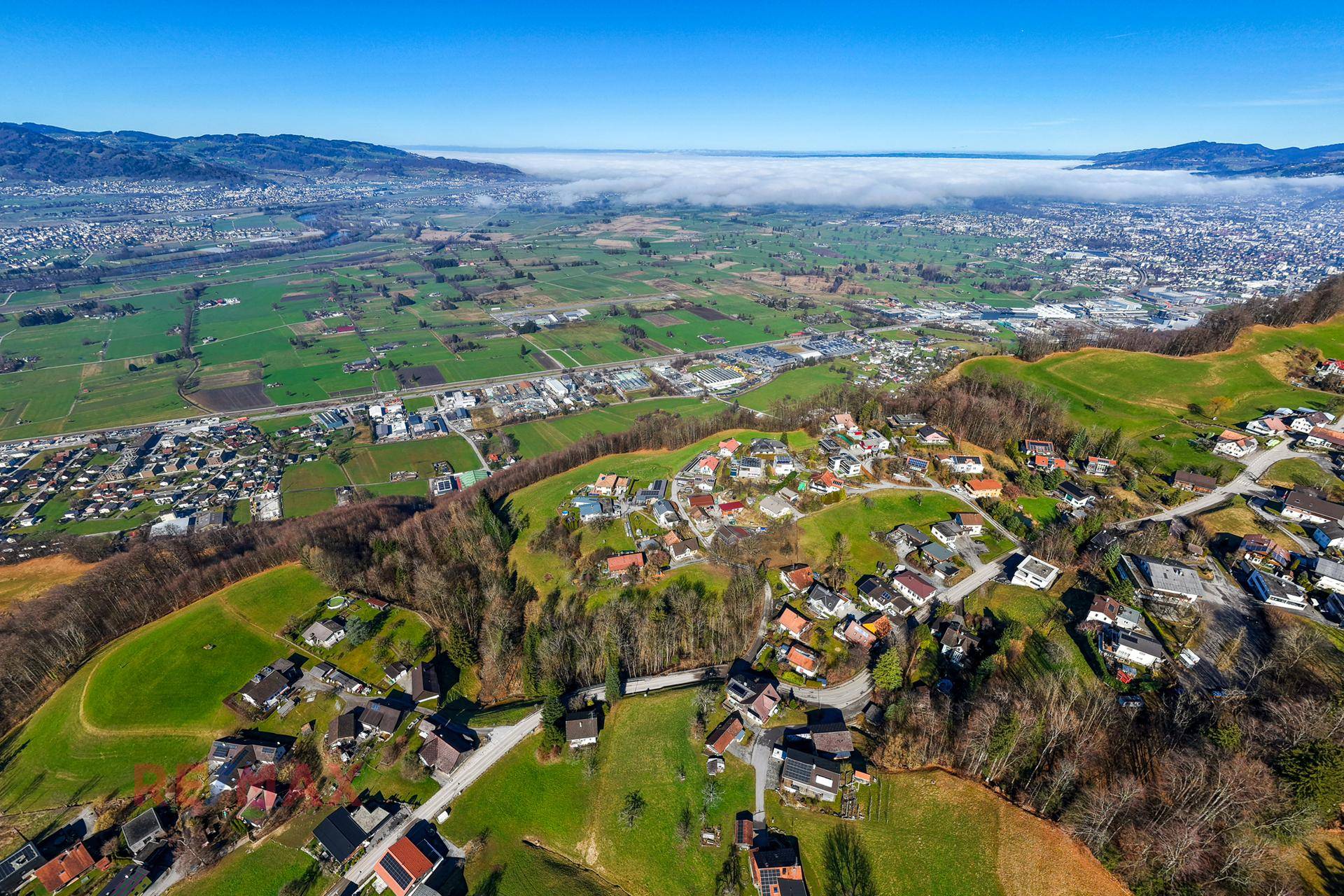 Umfassende Luftaufnahme des Tals mit weitläufiger Landschaft, Siedlungen und einer Stadt in der Ferne.