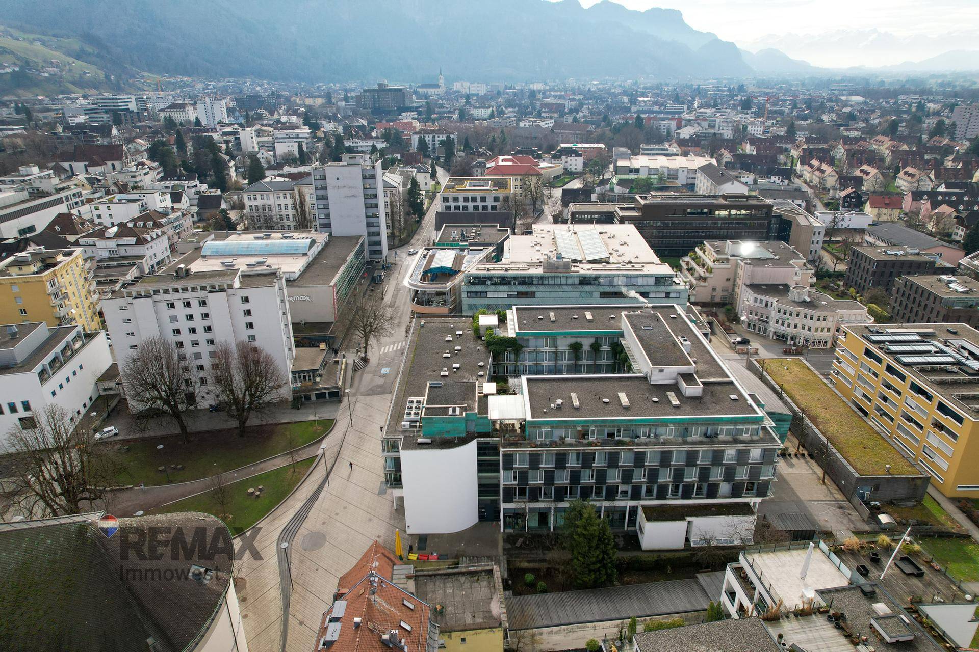 Weitläufige Luftaufnahme einer Stadt mit zahlreichen Gebäuden und einer beeindruckenden Bergkulisse im Hintergrund.