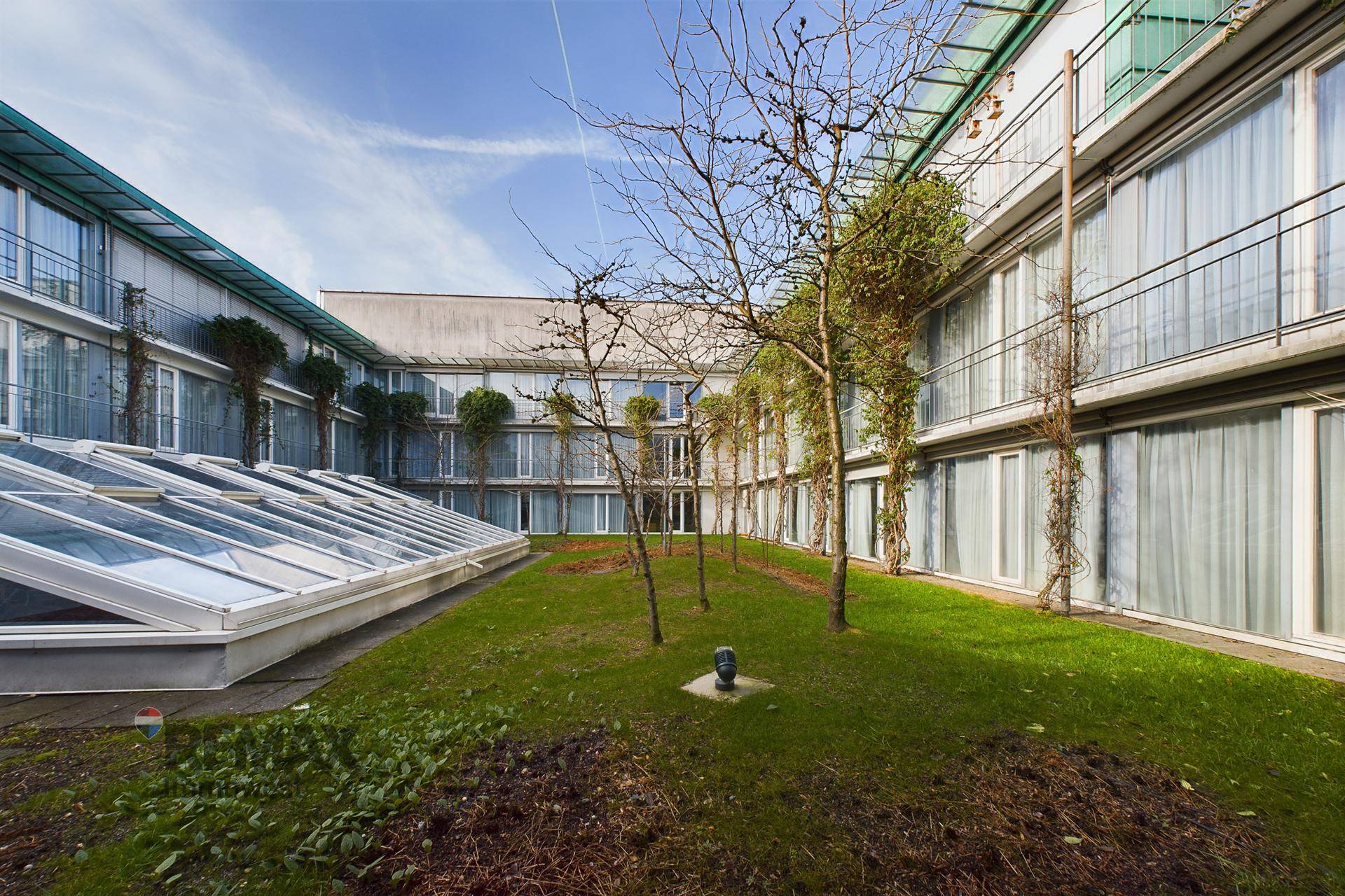Begrünter Innenhof mit Bäumen und Glasdächern, umgeben von den Fassaden des Gebäudekomplexes.