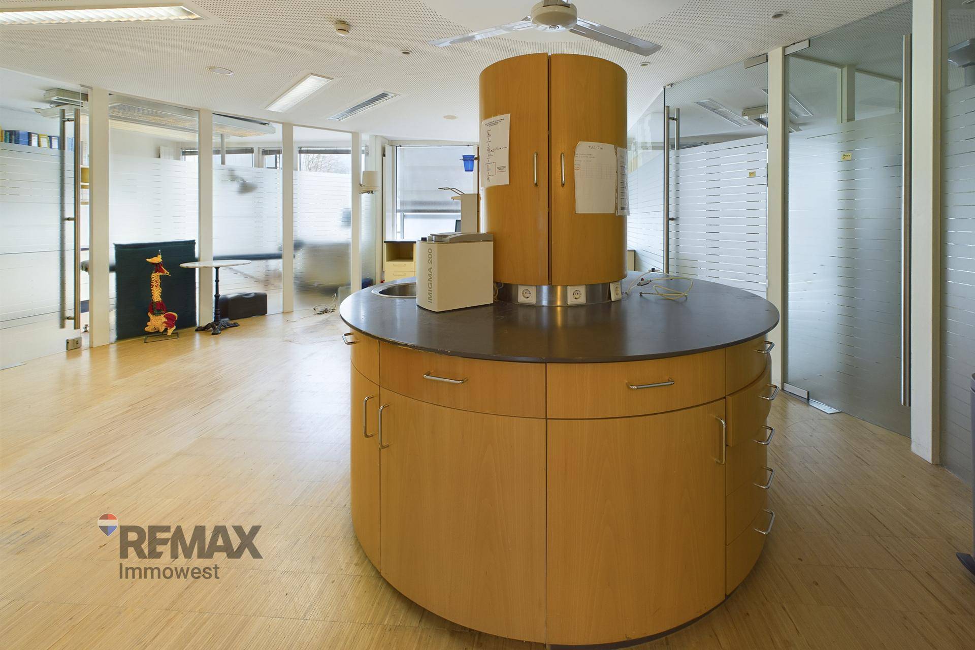 Offener Büroraum mit zentraler runder Arbeitsinsel, Glaswänden und Deckenventilator.