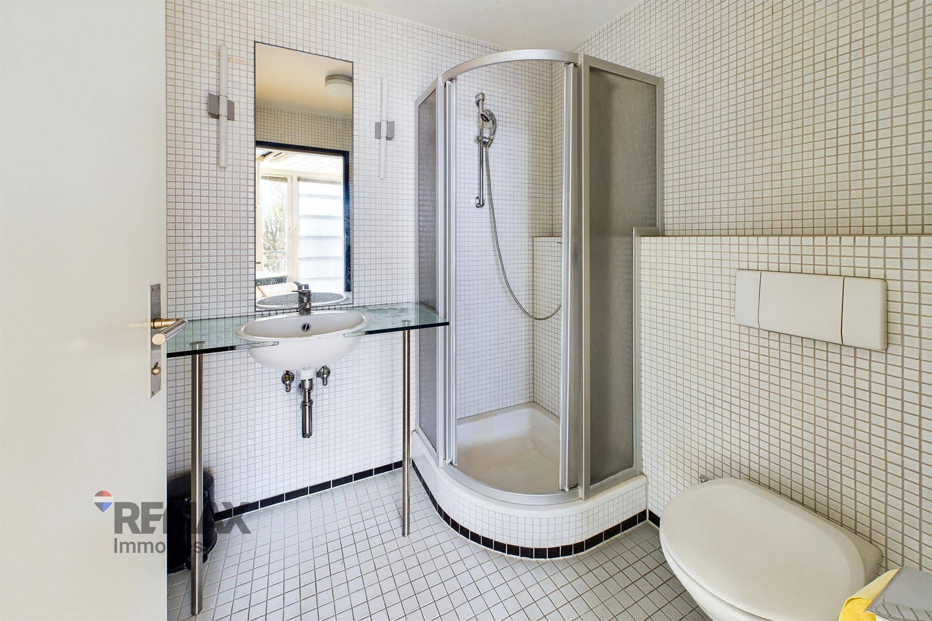 Badezimmer mit Duschkabine, Toilette und Waschbecken, komplett gefliest in Weiß und Schwarz.