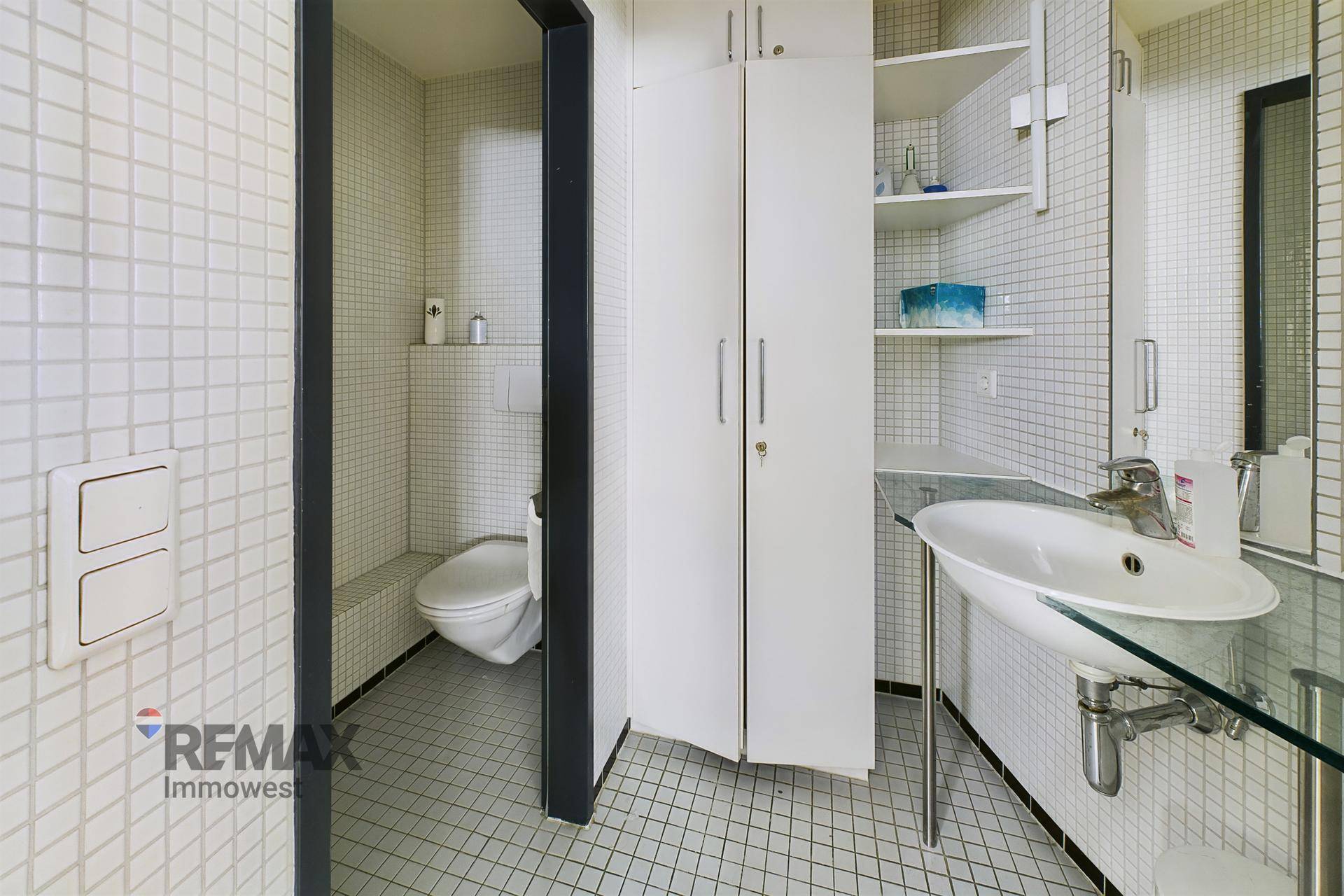 Badezimmer mit Waschbecken, Toilette und Einbauschränken, vollständig mit kleinen Fliesen versehen.