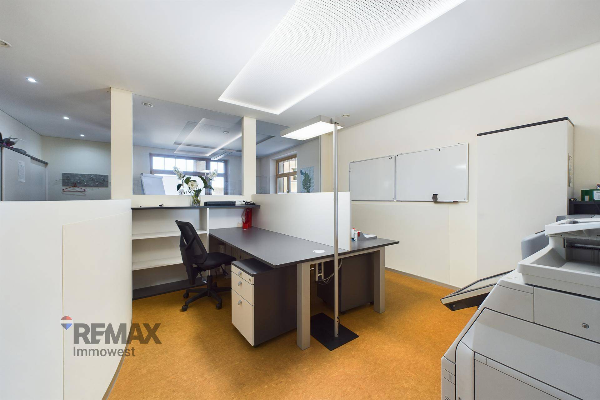 Moderner Arbeitsplatz in einem Büro mit Schreibtisch, Bürostuhl, Whiteboards und Linoleumboden.
