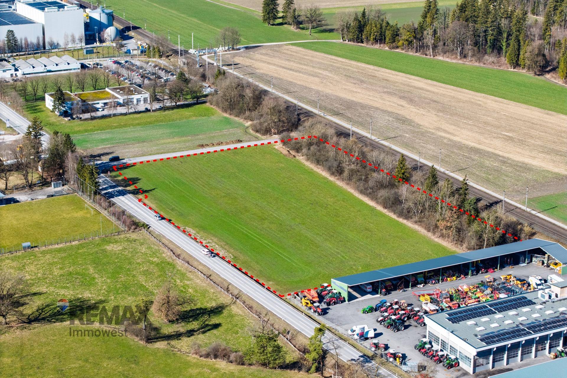 Luftaufnahme eines weitläufigen Grundstücks mit grünen Feldern, umgeben von Straßen und Industriegebäuden.