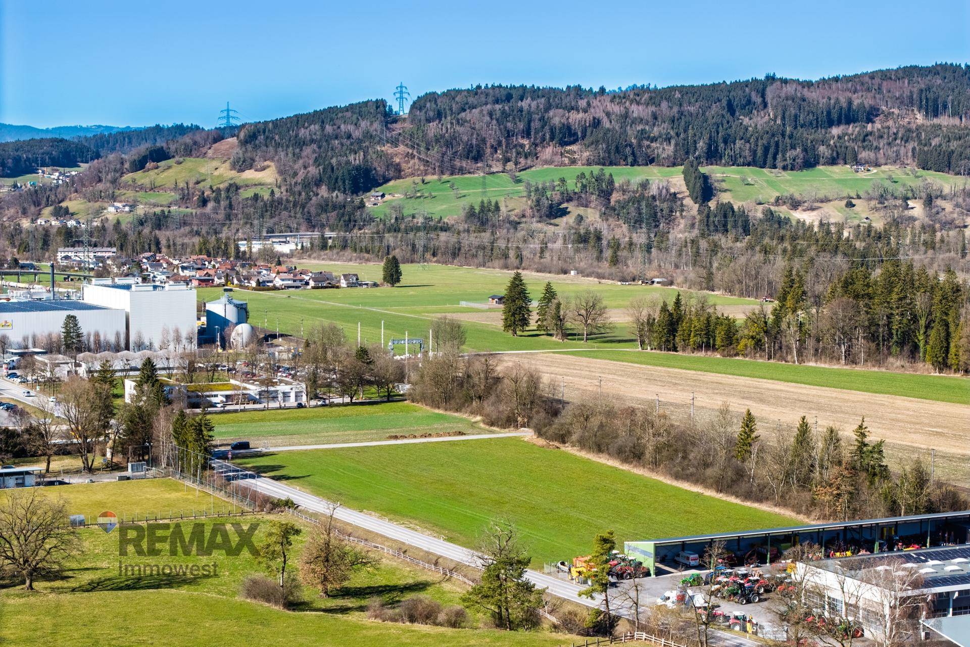 Panoramische Luftaufnahme der ländlichen Umgebung mit grünen Hügeln, Feldern und verstreuten Gebäuden.