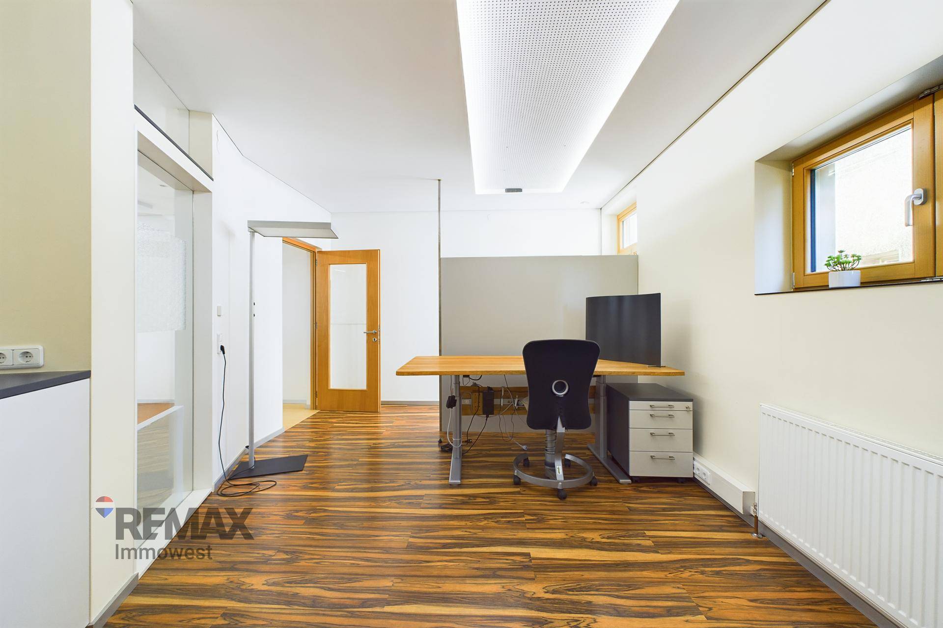 Büroarbeitsplatz mit Holzboden, Schreibtisch und Deckenbeleuchtung, gut beleuchtet.