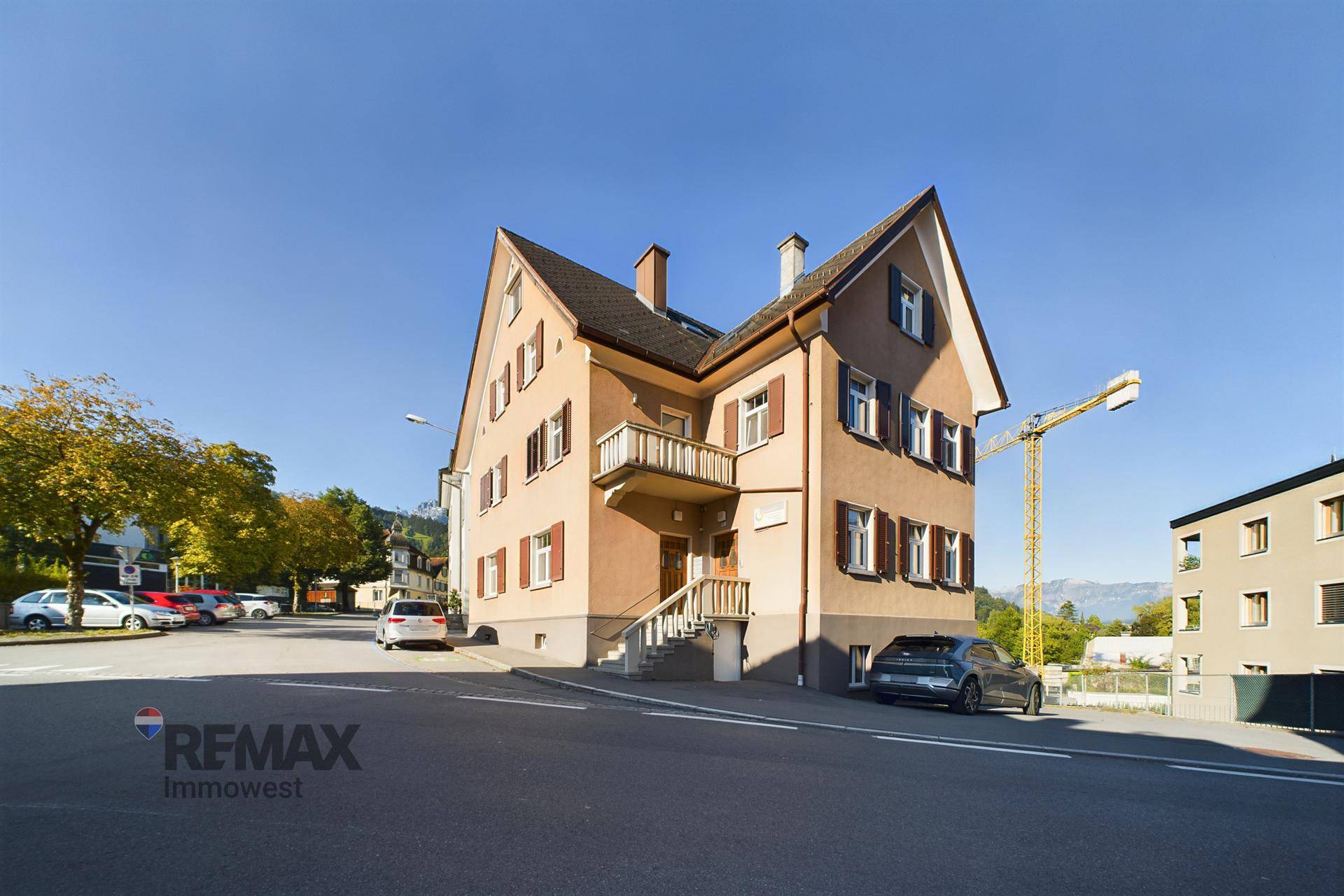 Historisches Gebäude an einer Straße mit Parkplätzen und einem Kran im Hintergrund.
