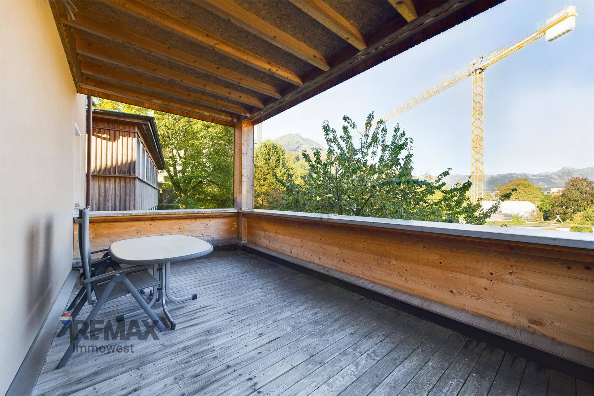 Überdachter Holzbalkon mit Sitzgelegenheiten und Blick auf Bäume und Berge.