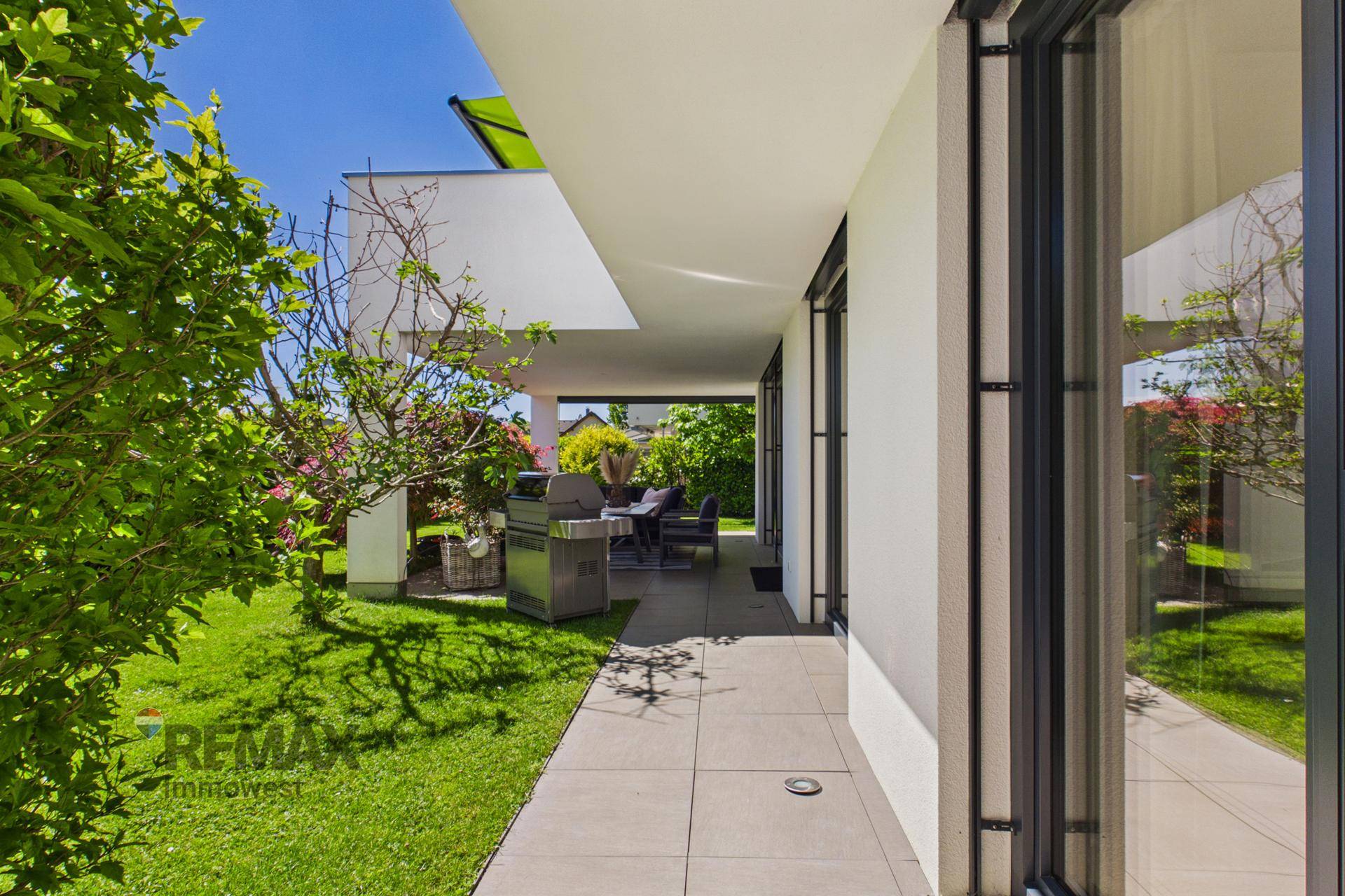 Lange, geflieste Terrasse entlang des Hauses mit Grillbereich und Zugang zum Garten.