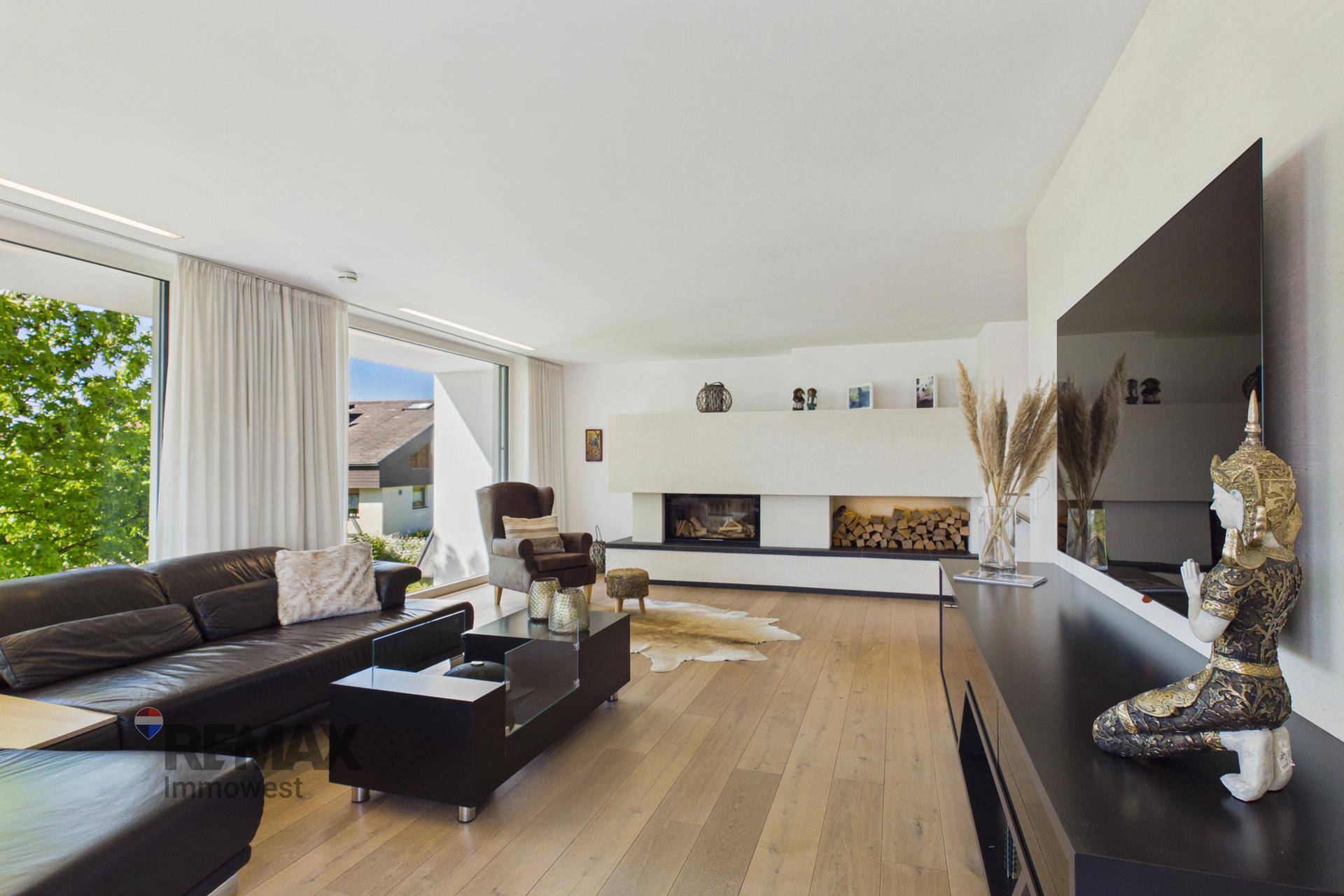 Großzügiges Wohnzimmer mit Holzboden, modernem Kamin und großen Fenstern.
