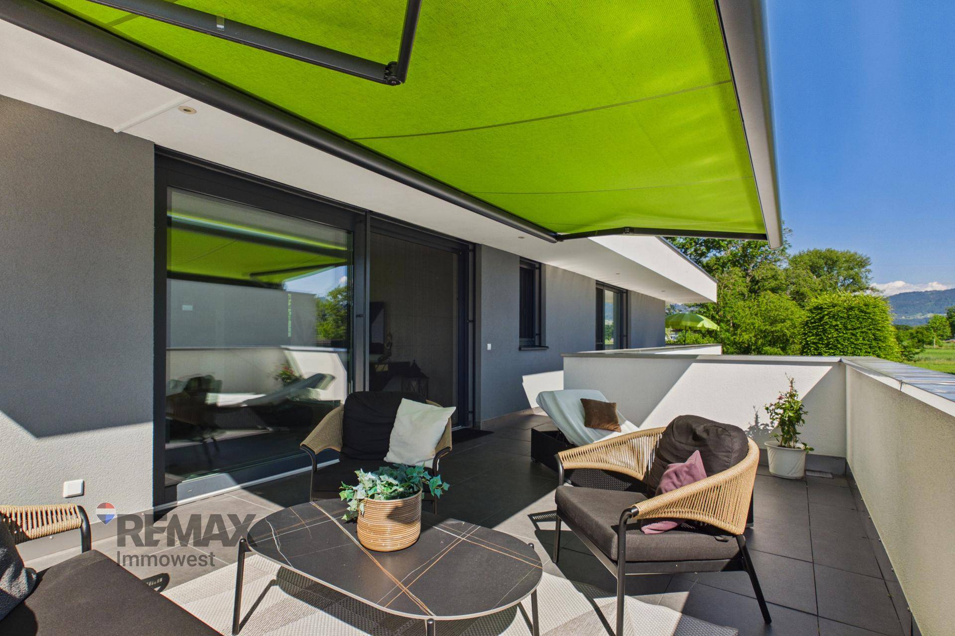 Geräumiger Balkon mit moderner Möblierung, grüner Markise und weitem Ausblick.