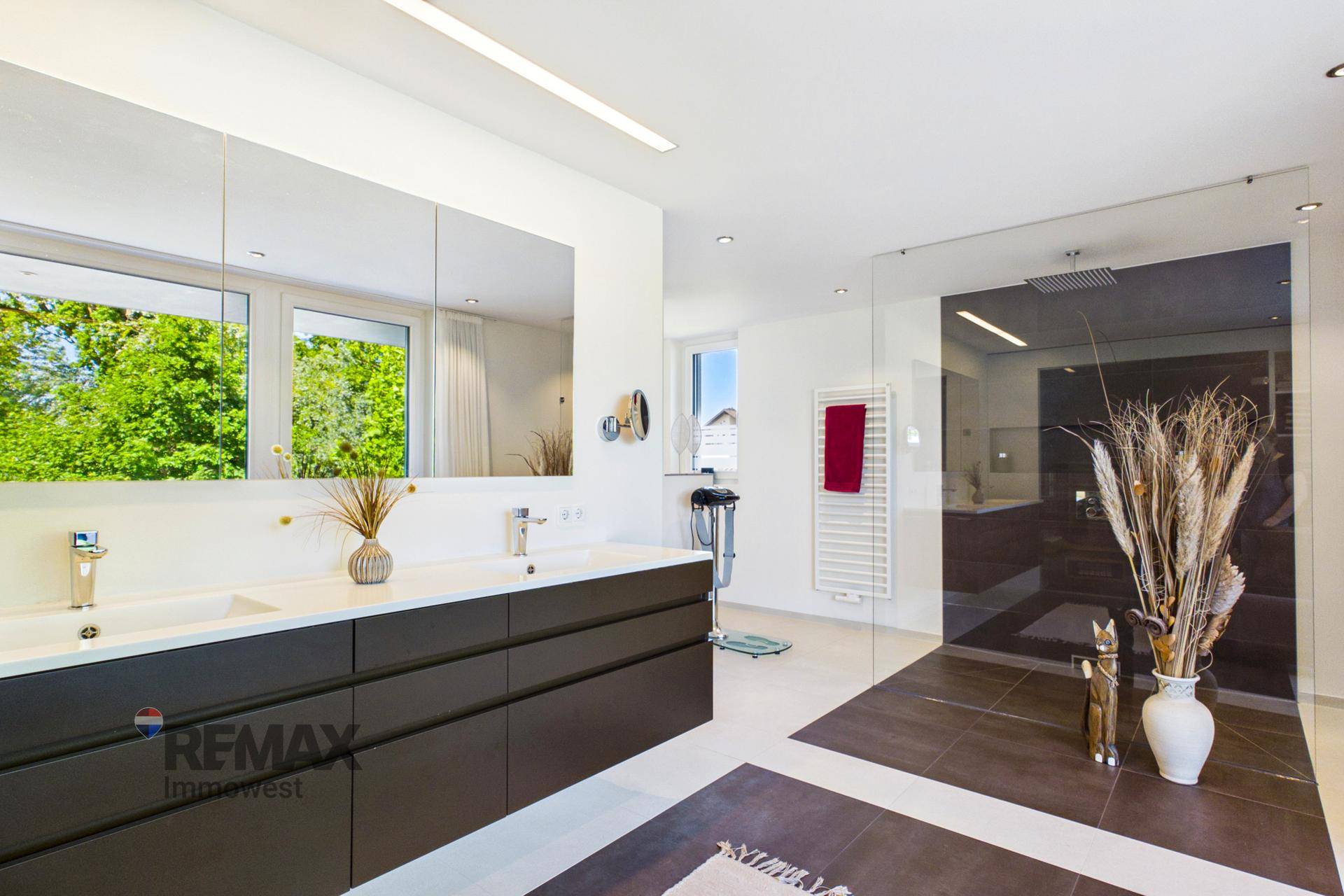 Modernes Badezimmer mit Doppelwaschbecken, großer Dusche und Fenster mit Blick ins Grüne.