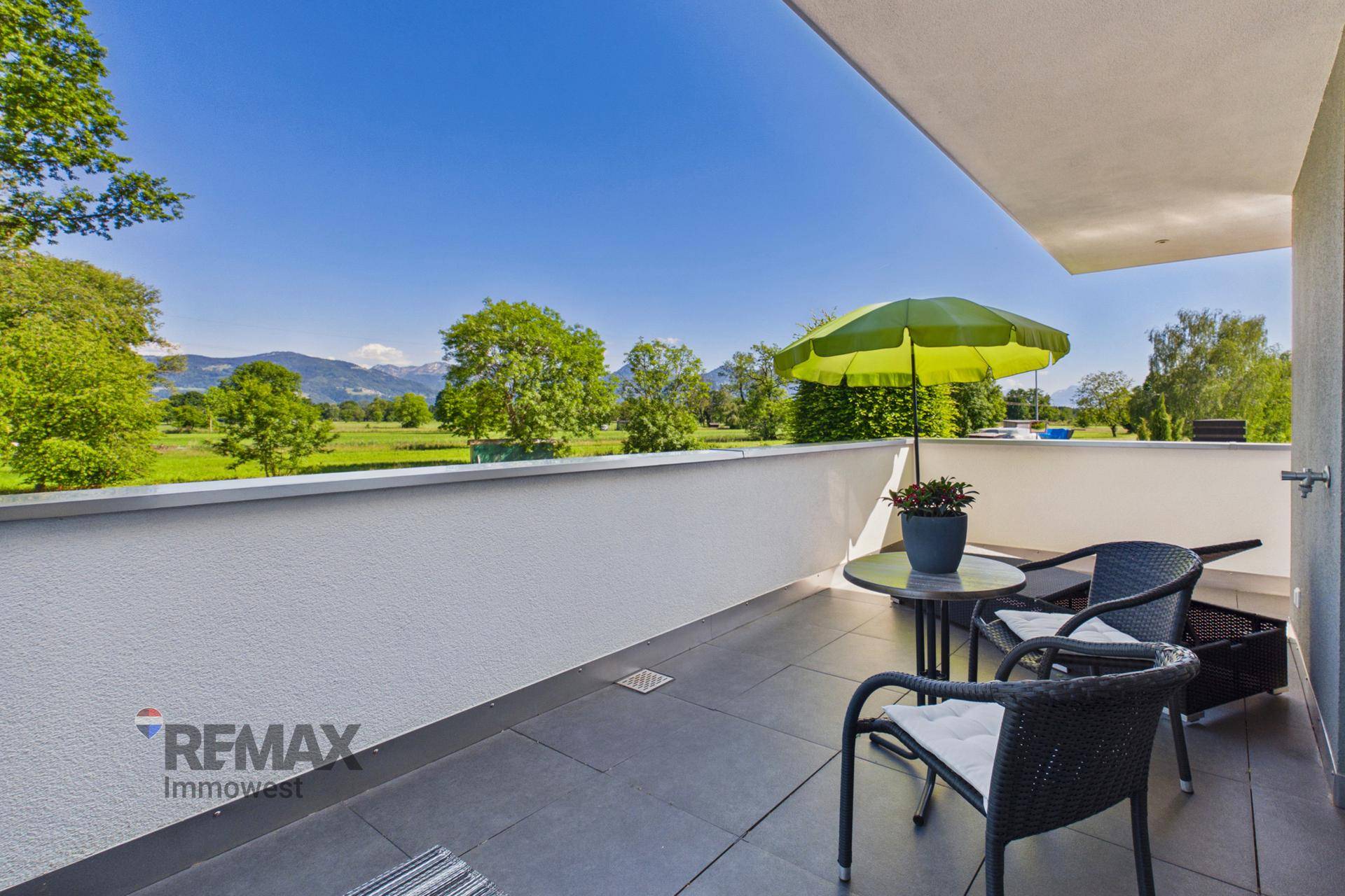 Heller Balkon mit Sitzgelegenheiten, Sonnenschirm und Panoramablick auf die Berge und Natur.