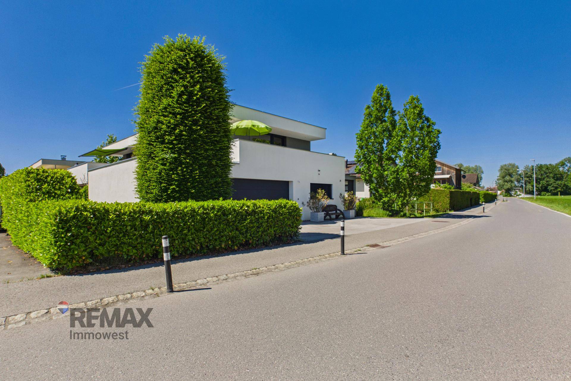 Ansicht des modernen Hauses von der Straße mit gepflegter Hecke und Bäumen.