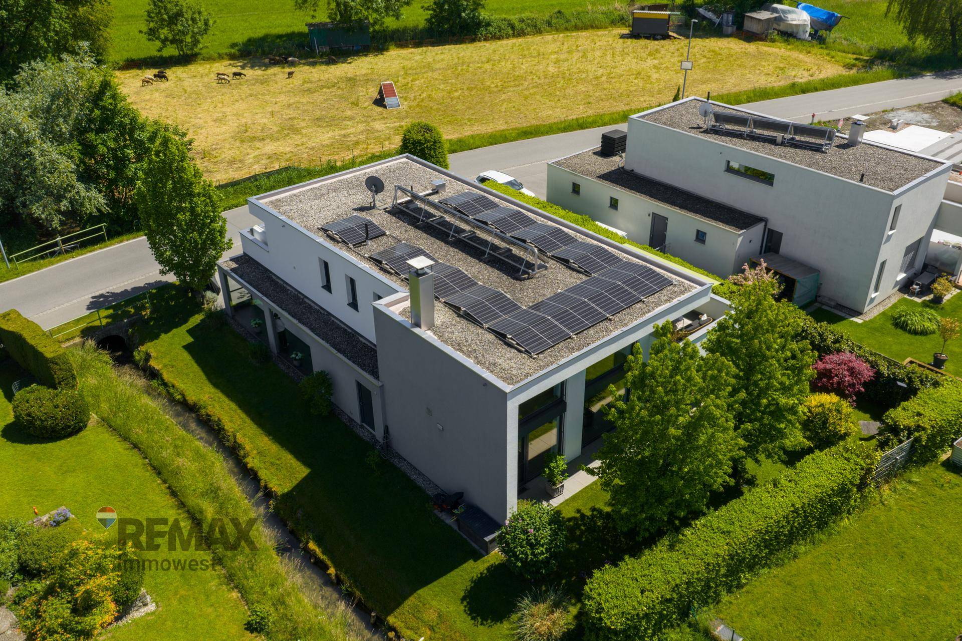Luftaufnahme eines modernen Hauses mit Flachdach, Photovoltaikanlage und gepflegtem Garten.