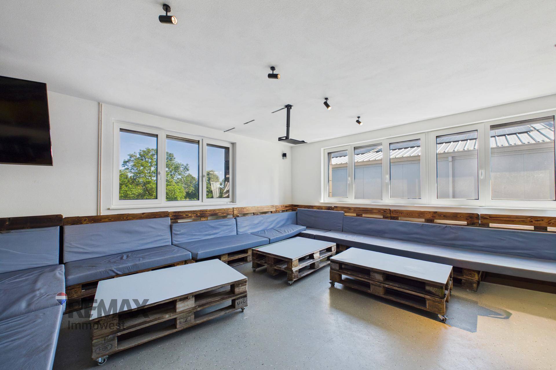 Entspannter Loungebereich mit Palettenmöbeln und blauen Kissen, hell durch große Fenster.