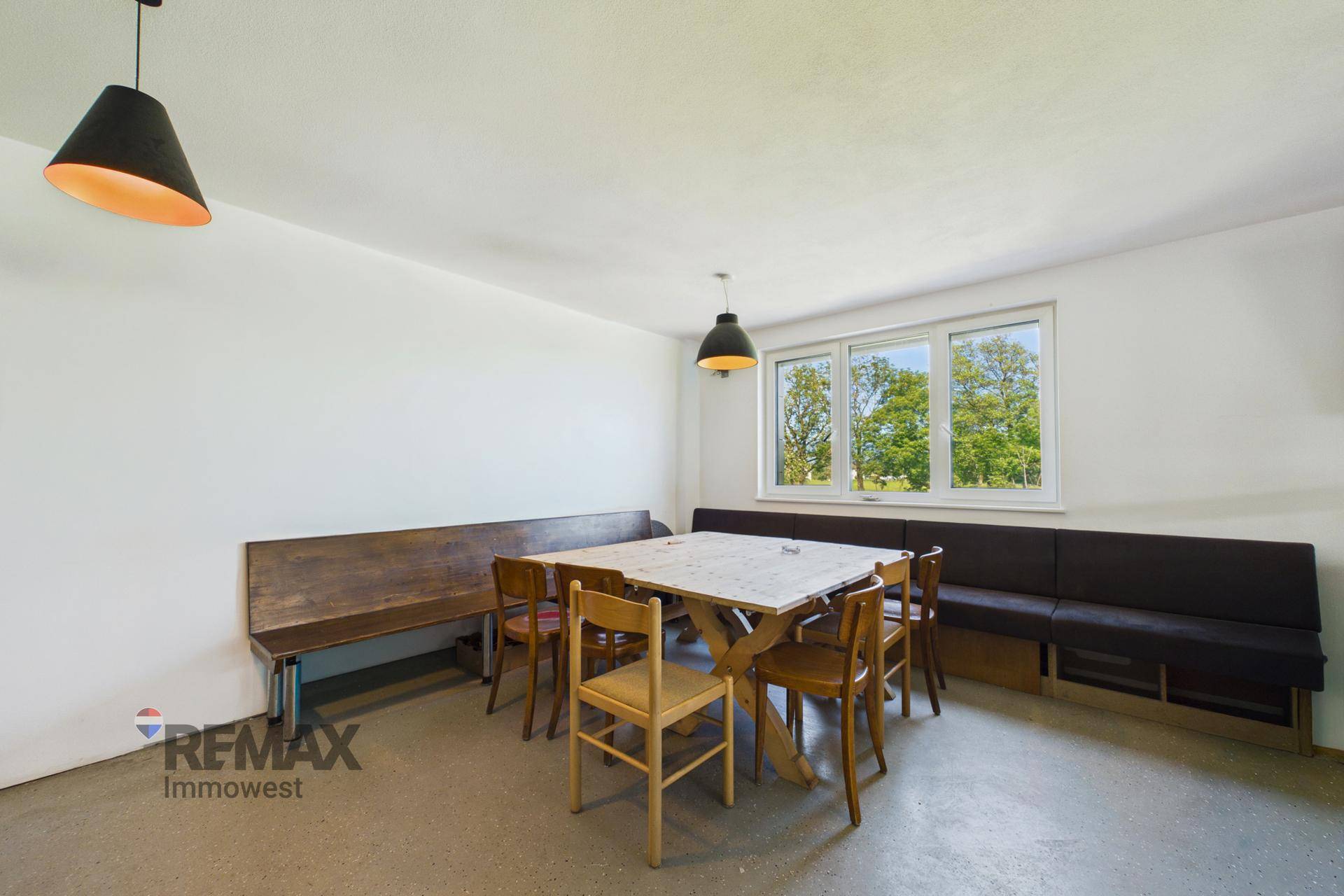 Gemütlicher Essbereich mit Holztischen und Bänken, hell durch ein großes Fenster mit Blick ins Grüne.