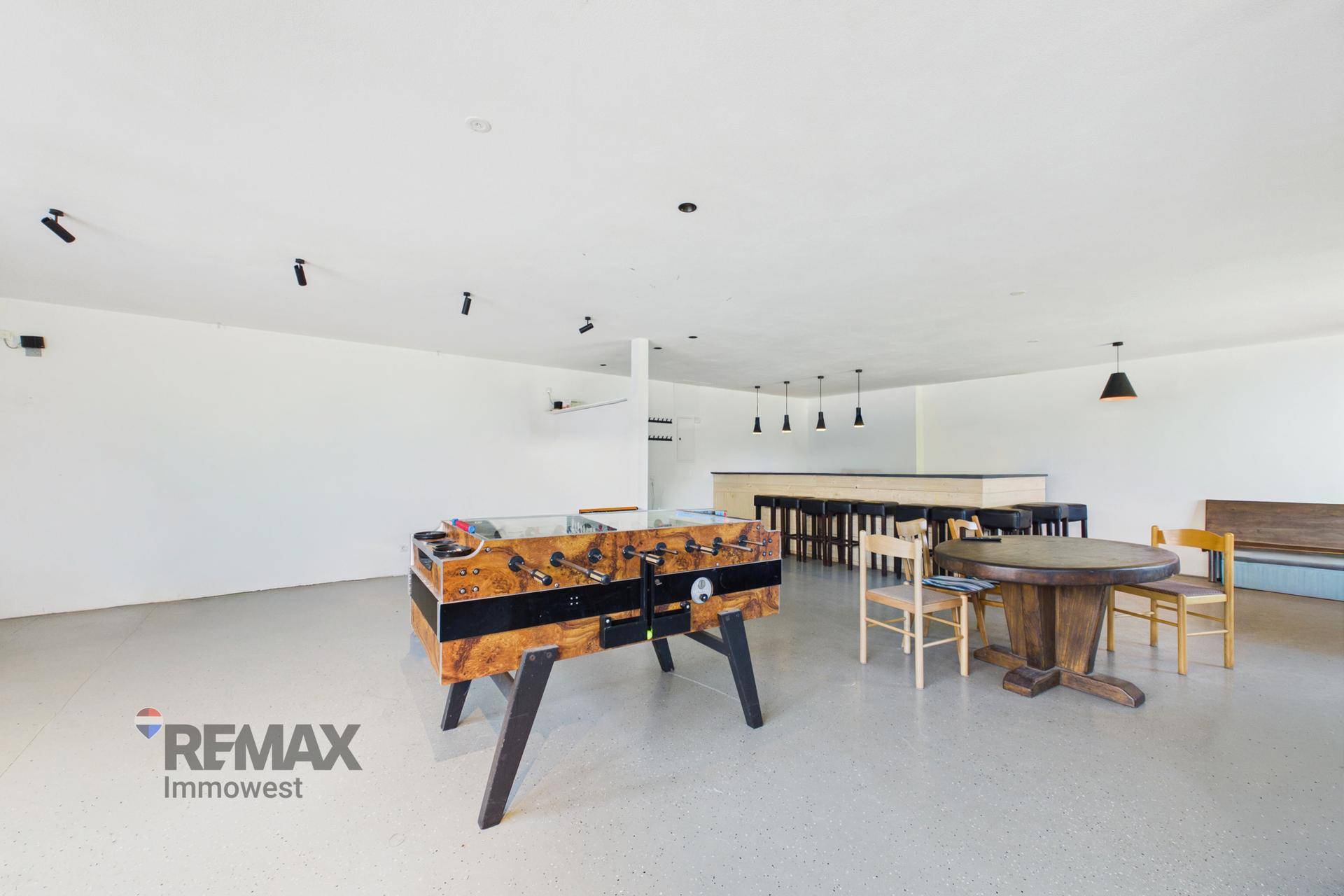 Großer Freizeitraum mit Tischfußball und runden Esstischen, die Bar ist im Hintergrund sichtbar.
