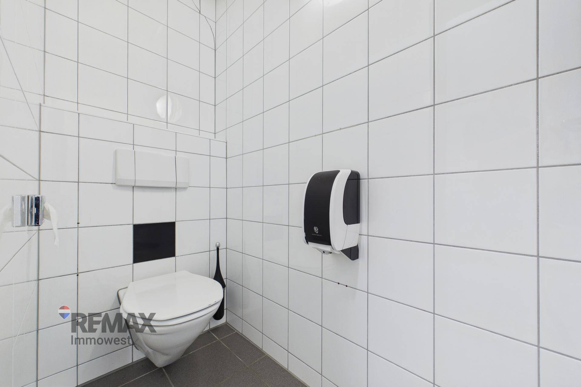 Toilettenkabine in einem öffentlichen Waschraum mit weißen Fliesen und Wand-WC.