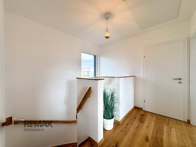 Heller Flur mit Holztreppe, Fenster und modernem Holzboden.