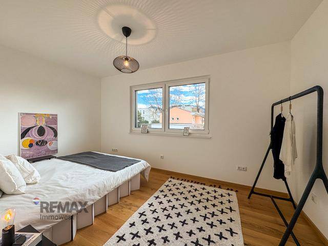 Gemütliches Schlafzimmer mit Holzboden, großem Fenster und moderner Einrichtung.