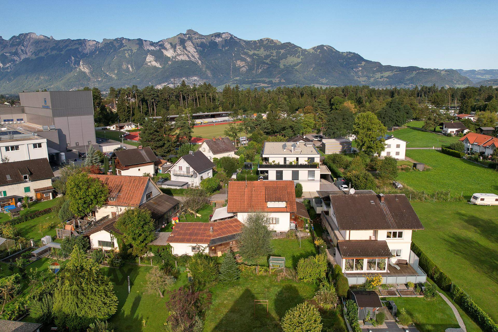 Weitläufige Luftaufnahme der Wohngegend mit Häusern, Grünflächen und Bergblick.