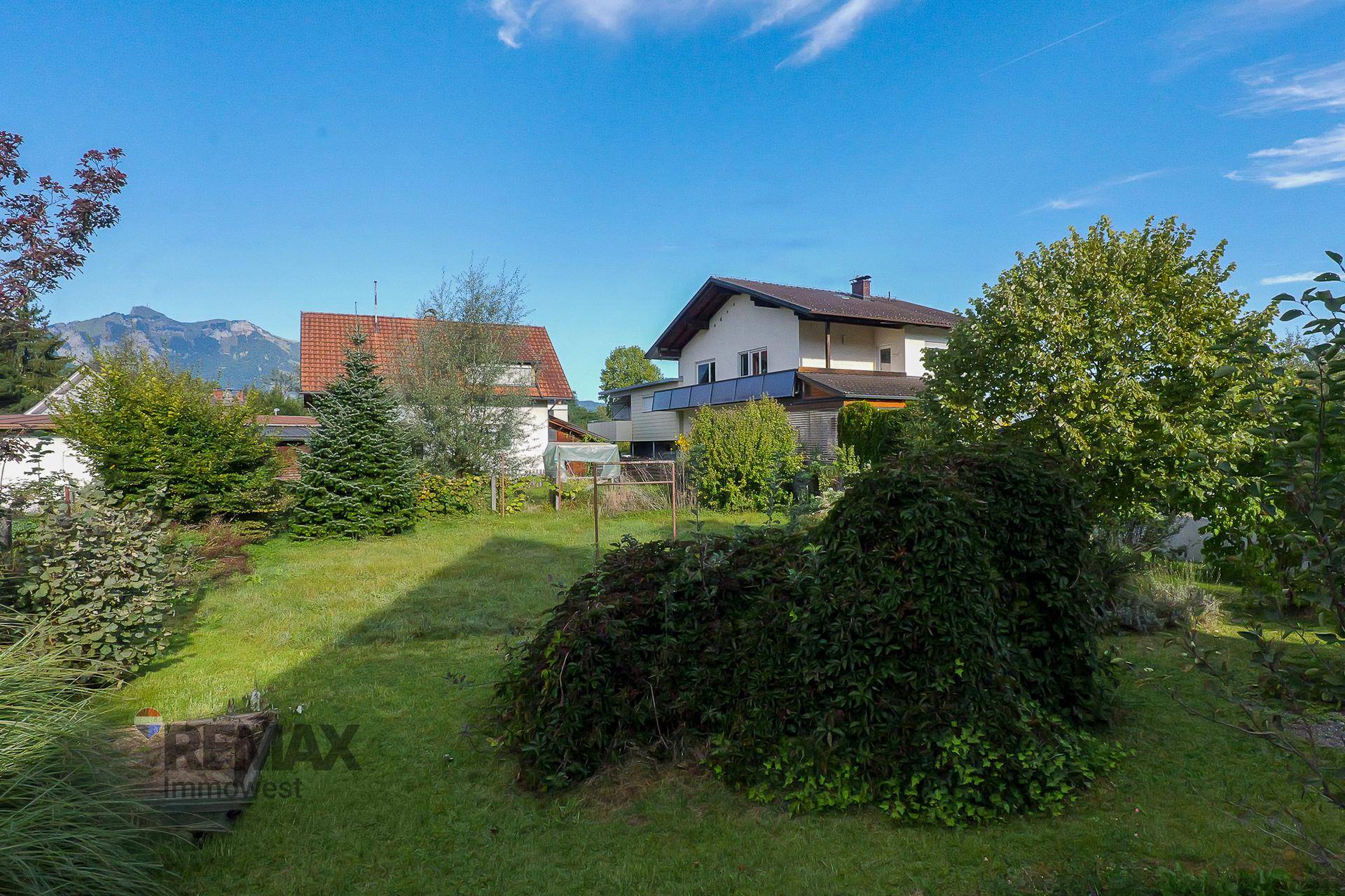Gepflegter Gartenbereich mit Rasen, Sträuchern und Blick auf die umliegenden Häuser und Berge.