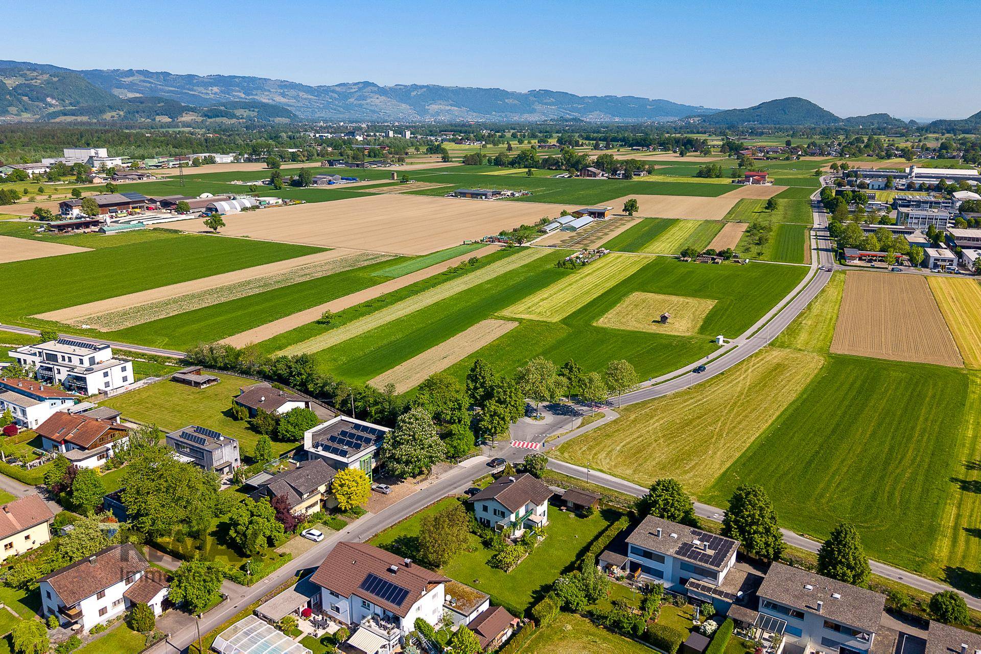 Weitwinkel-Luftaufnahme einer ländlichen Region mit Wohngebieten, Feldern und einer beeindruckenden Bergkulisse.
