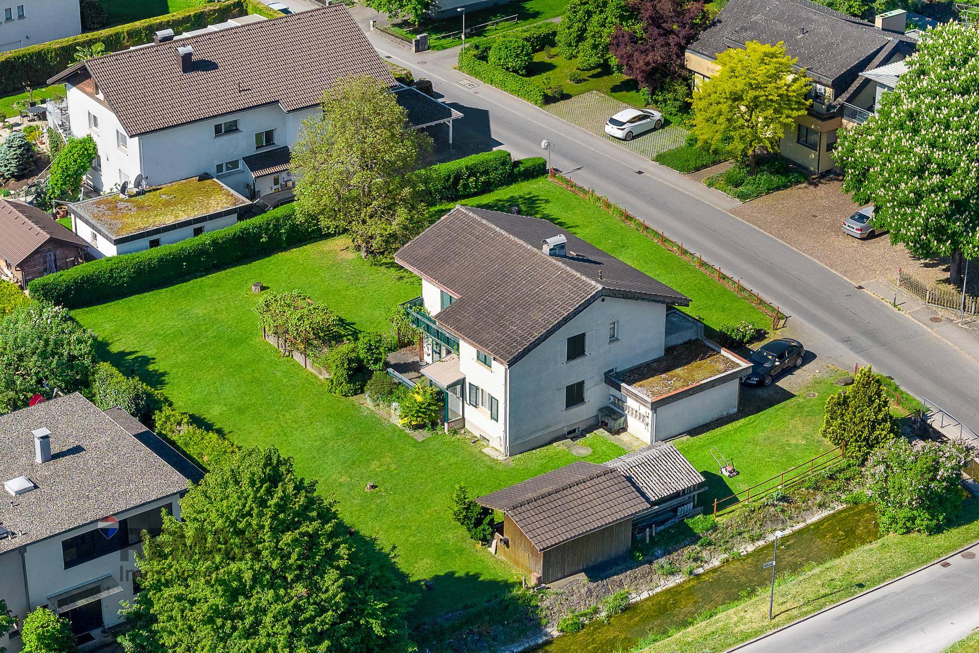 Vogelperspektive eines Einfamilienhauses mit weitläufigem Garten, umgeben von weiteren Wohnhäusern und Natur.